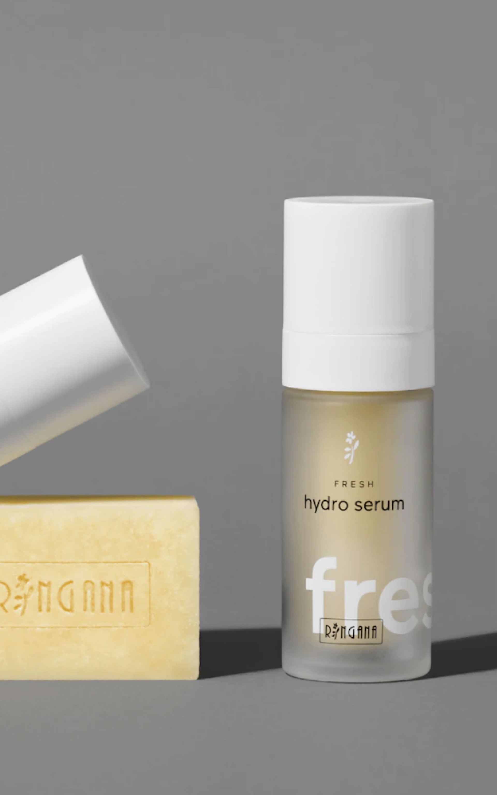 Ein "fresh hydro serum" der Marke RINGANA und eine gelbe Seife, beide auf einem grauen Hintergrund.