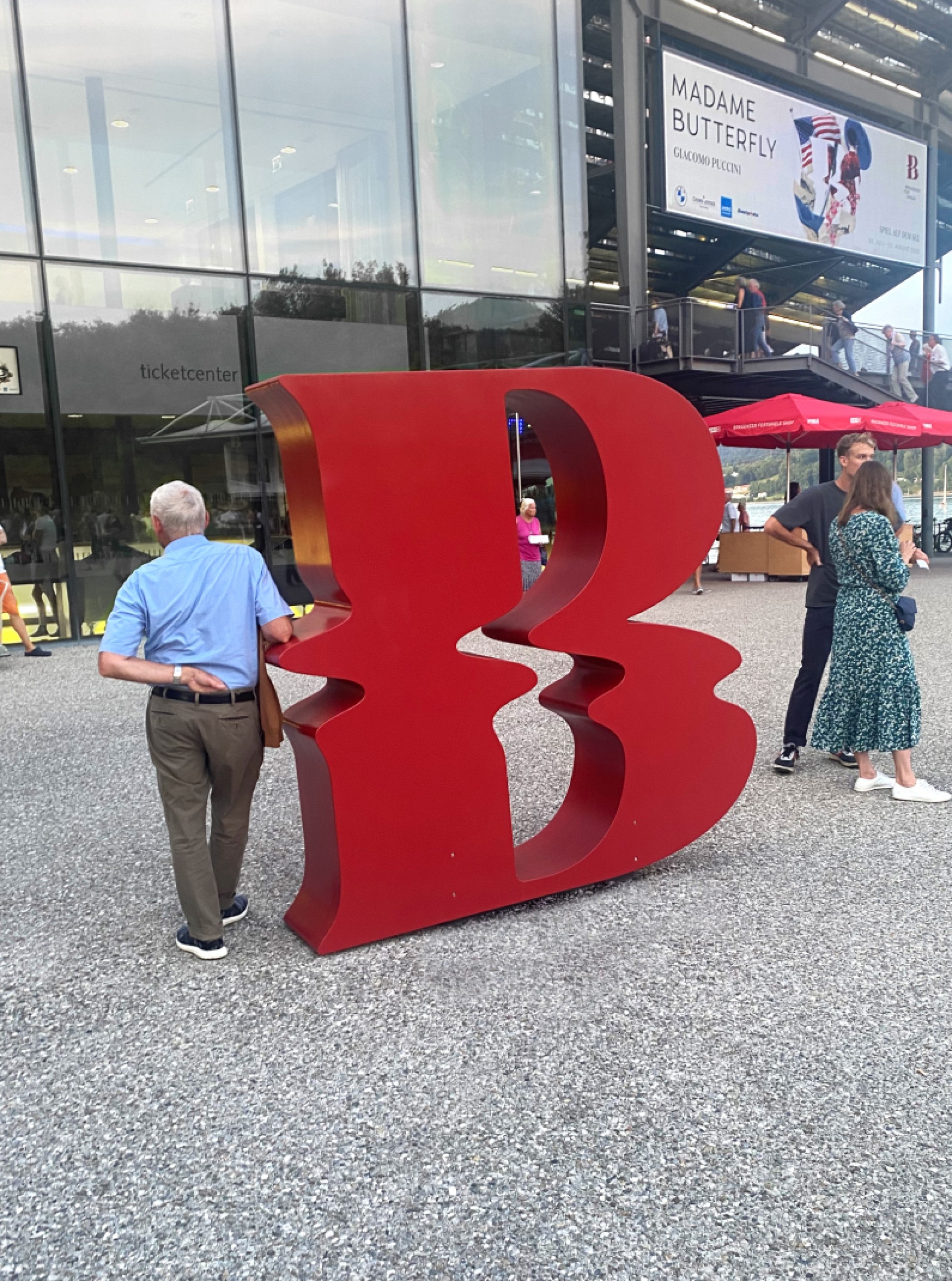 Rotes „B“ mit Publikum, Ticketcenter und einem Schild für „Madame Butterfly“ im Hintergrund.