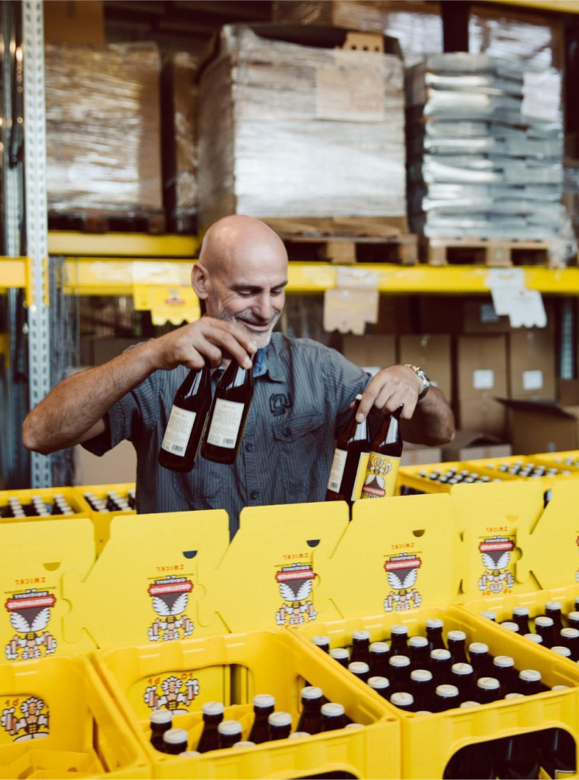 Ein Mann hält Zwickel-Bierflaschen vor gelben Bierkisten in einem Lagerhaus.