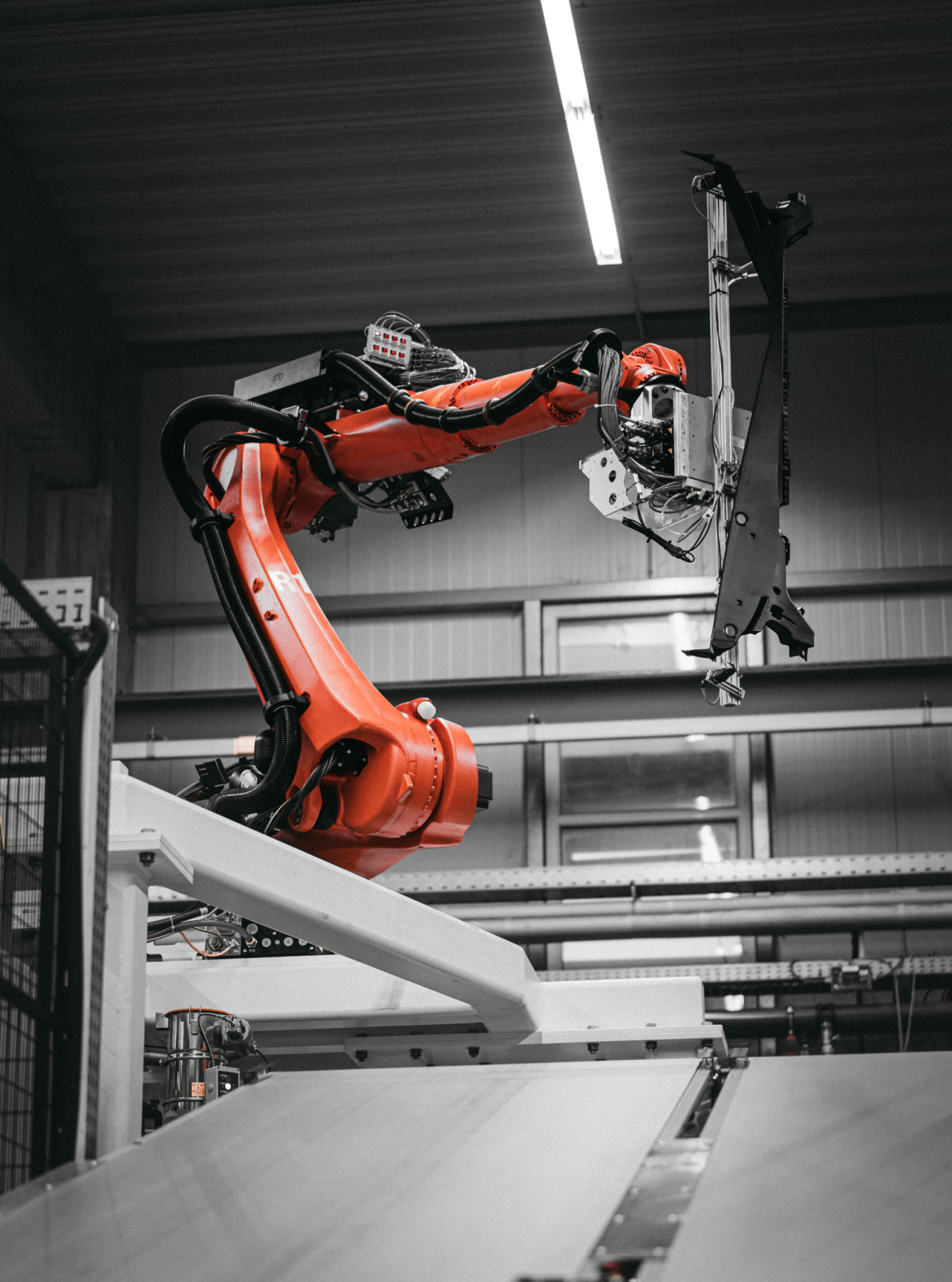 Ein orangefarbener Roboterarm in einer Produktionshalle, der einen schweren Gegenstand hält.