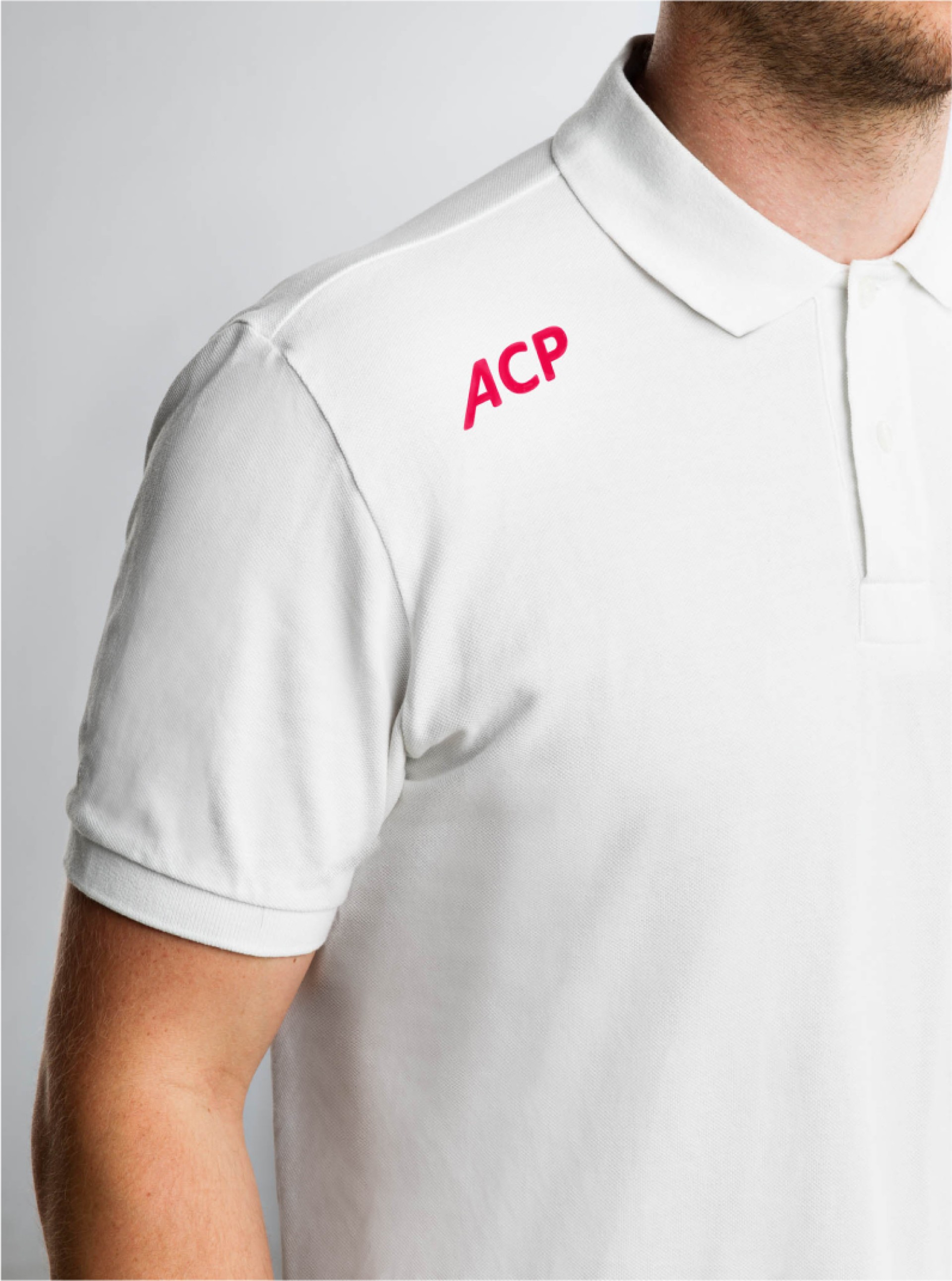 Ein Mann trägt ein weißes Polohemd mit rotem "ACP"-Logo auf der Brust.