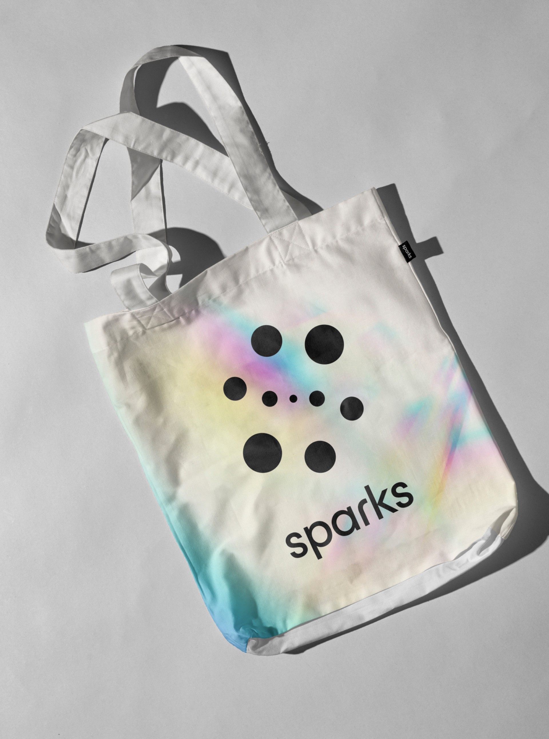 Weiße Tragetasche mit Regenbogenmuster, schwarzem Kreisdesign und Text "sparks".