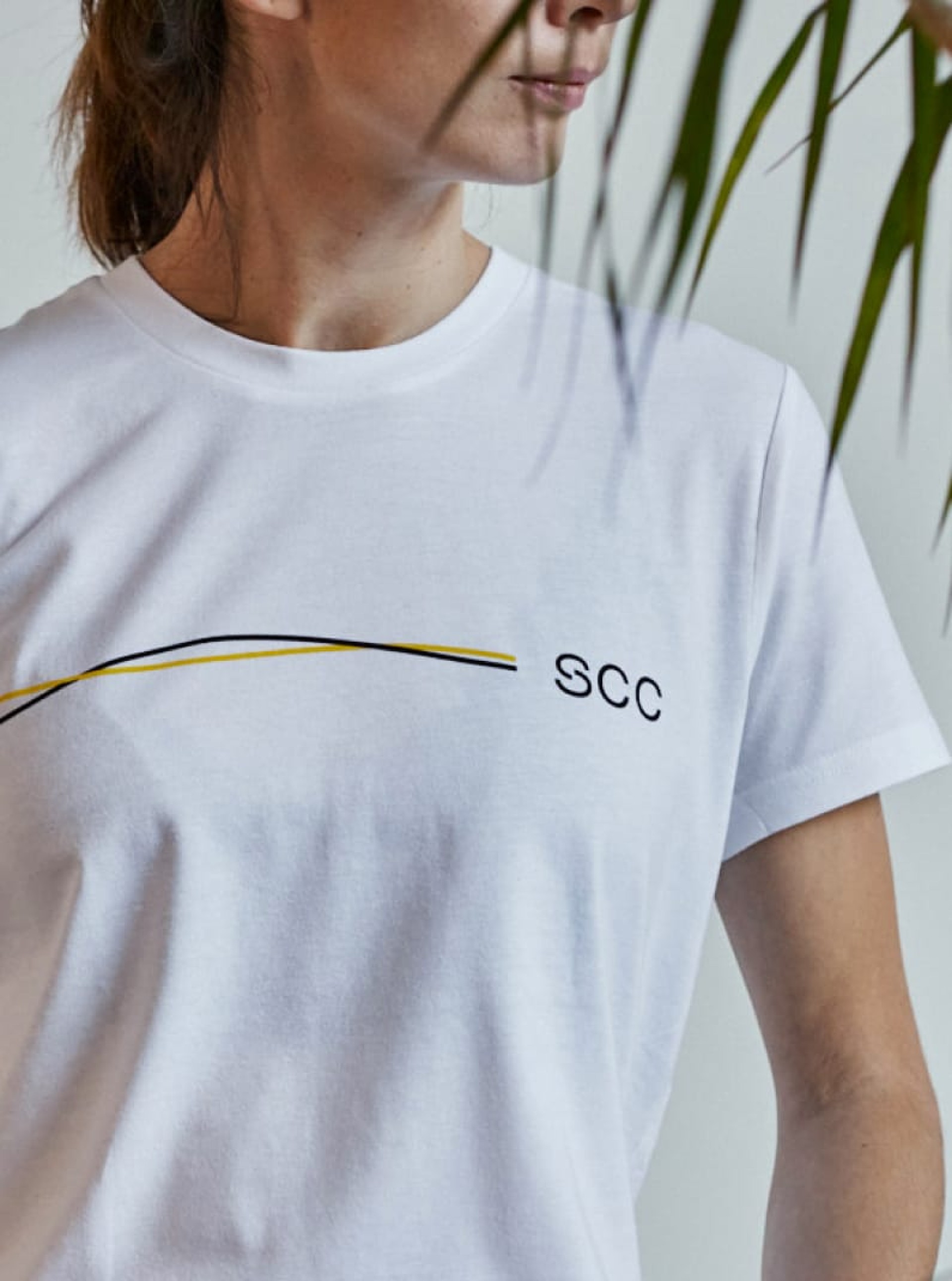 Frau in weißem SCC T-Shirt mit gelbem und schwarzem Streifen.