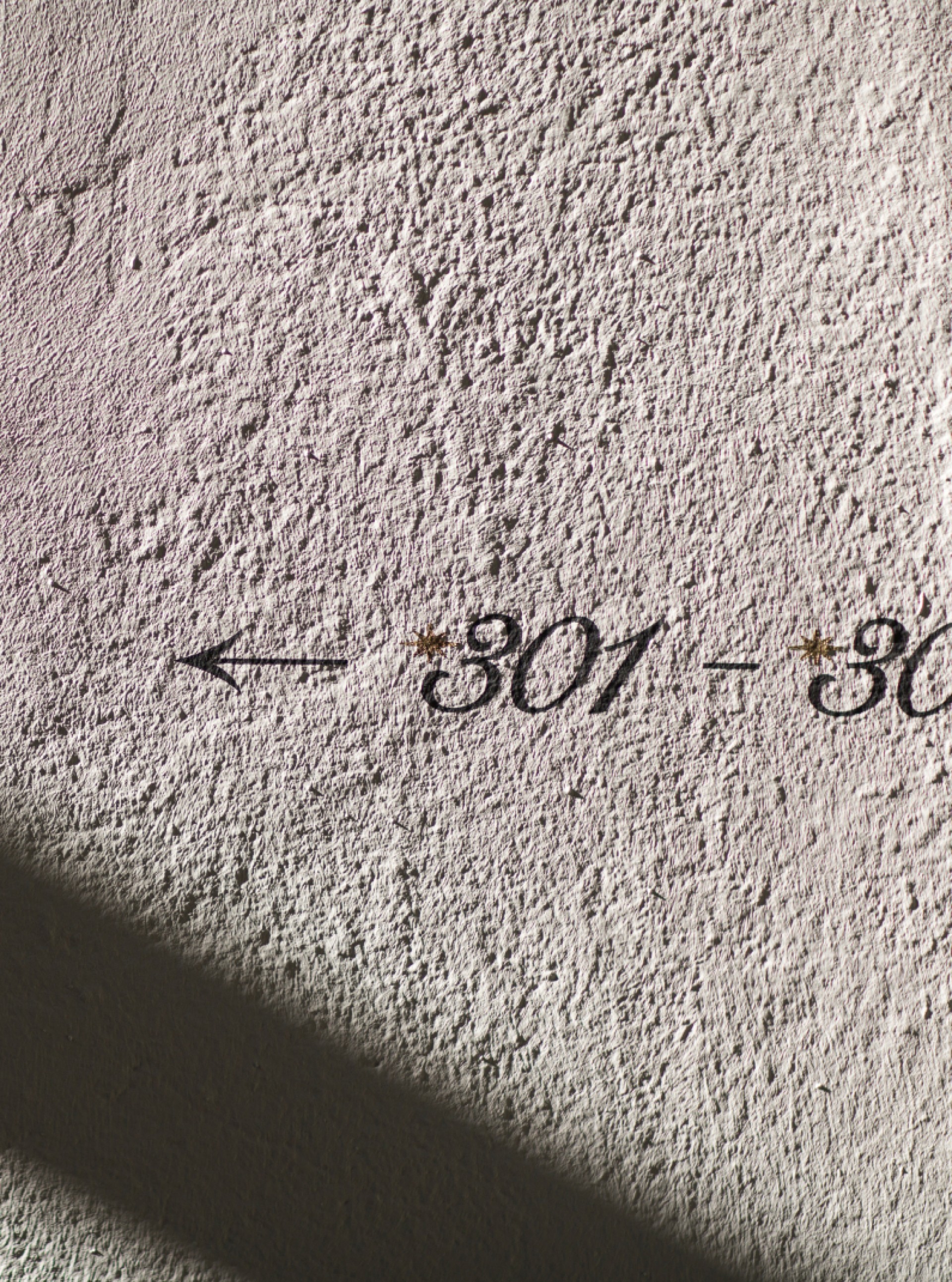 Rauhe Wand zeigt die Aufschrift "301-30" mit Sternen, ein Pfeil nach links und einen Schatten.