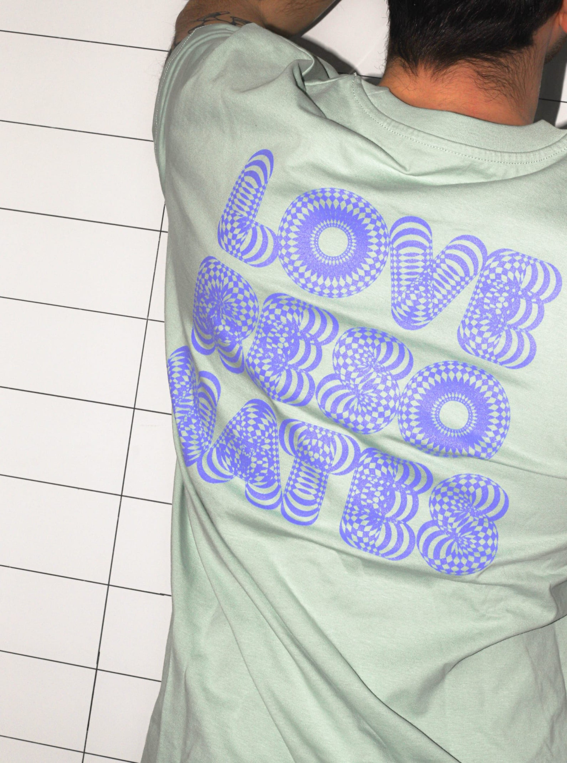 Mann mit "Love Booo hates" Hemd, auf einem weißen Fliesenboden.