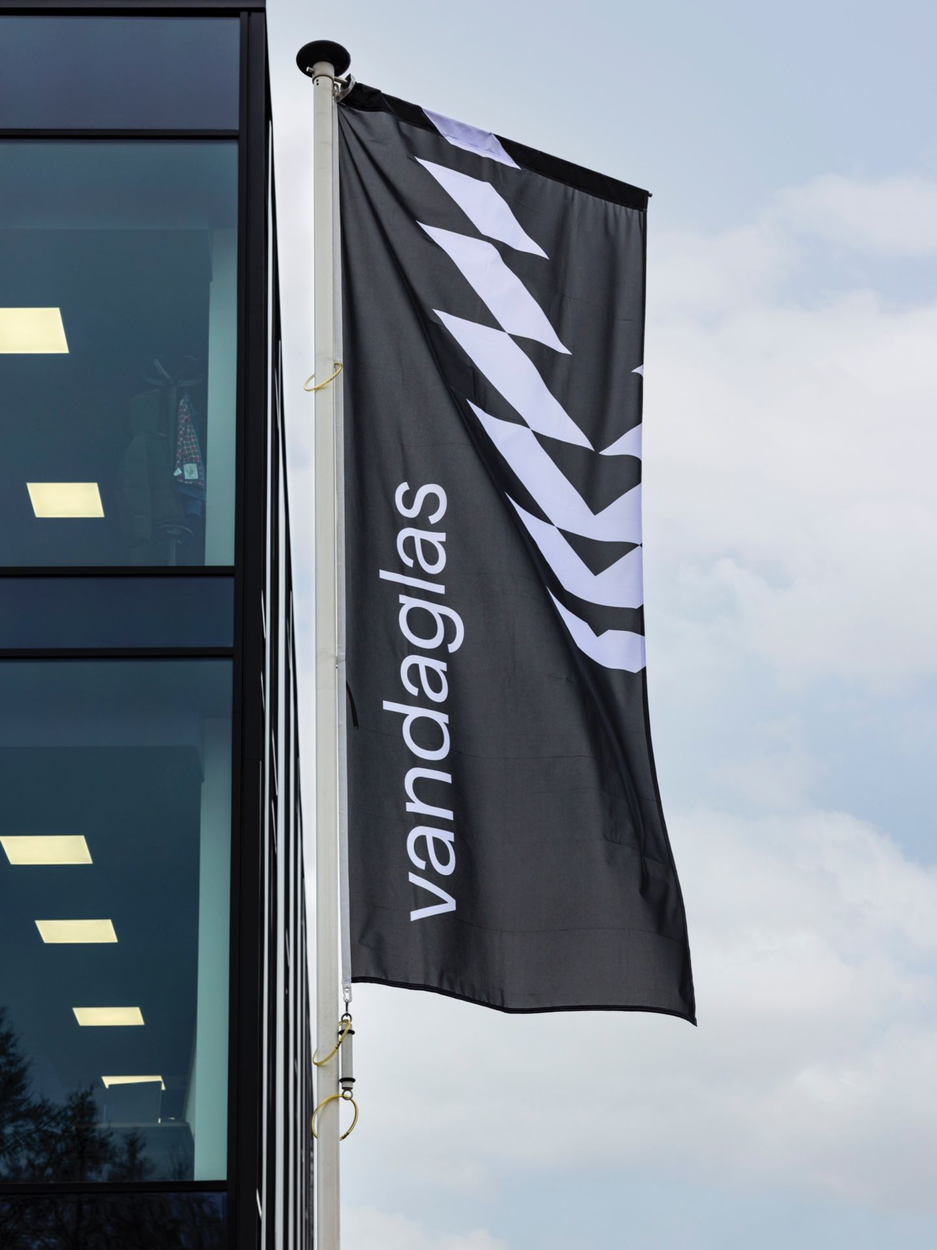 Schwarze Vandaglas-Flagge mit weißen Chevronen und der Aufschrift "vandaglas" vor einem Gebäude.