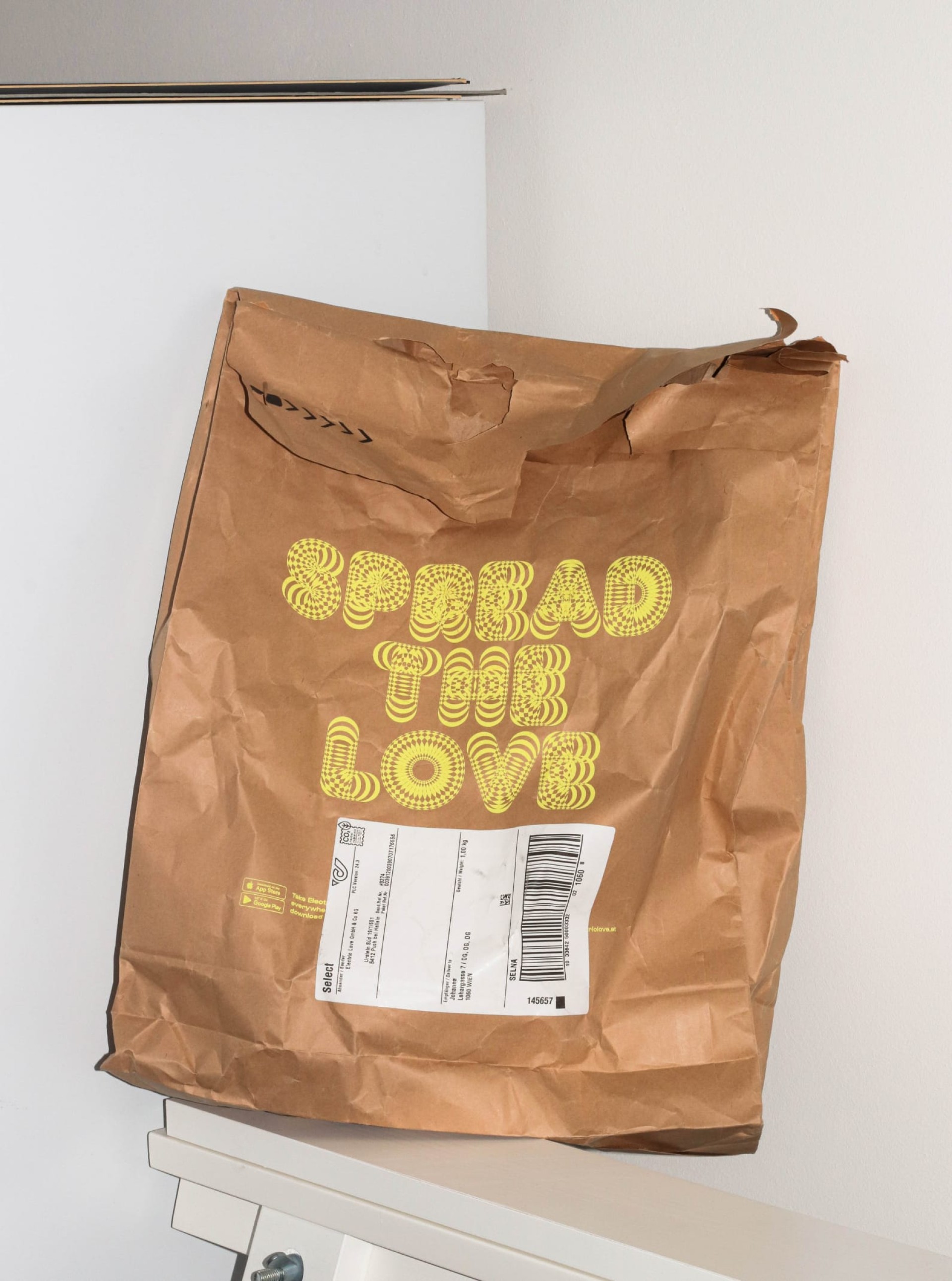 Eine braune Einkaufstasche mit dem Text "SPREAD THE LOVE" in gelber Schrift auf der Vorderseite.