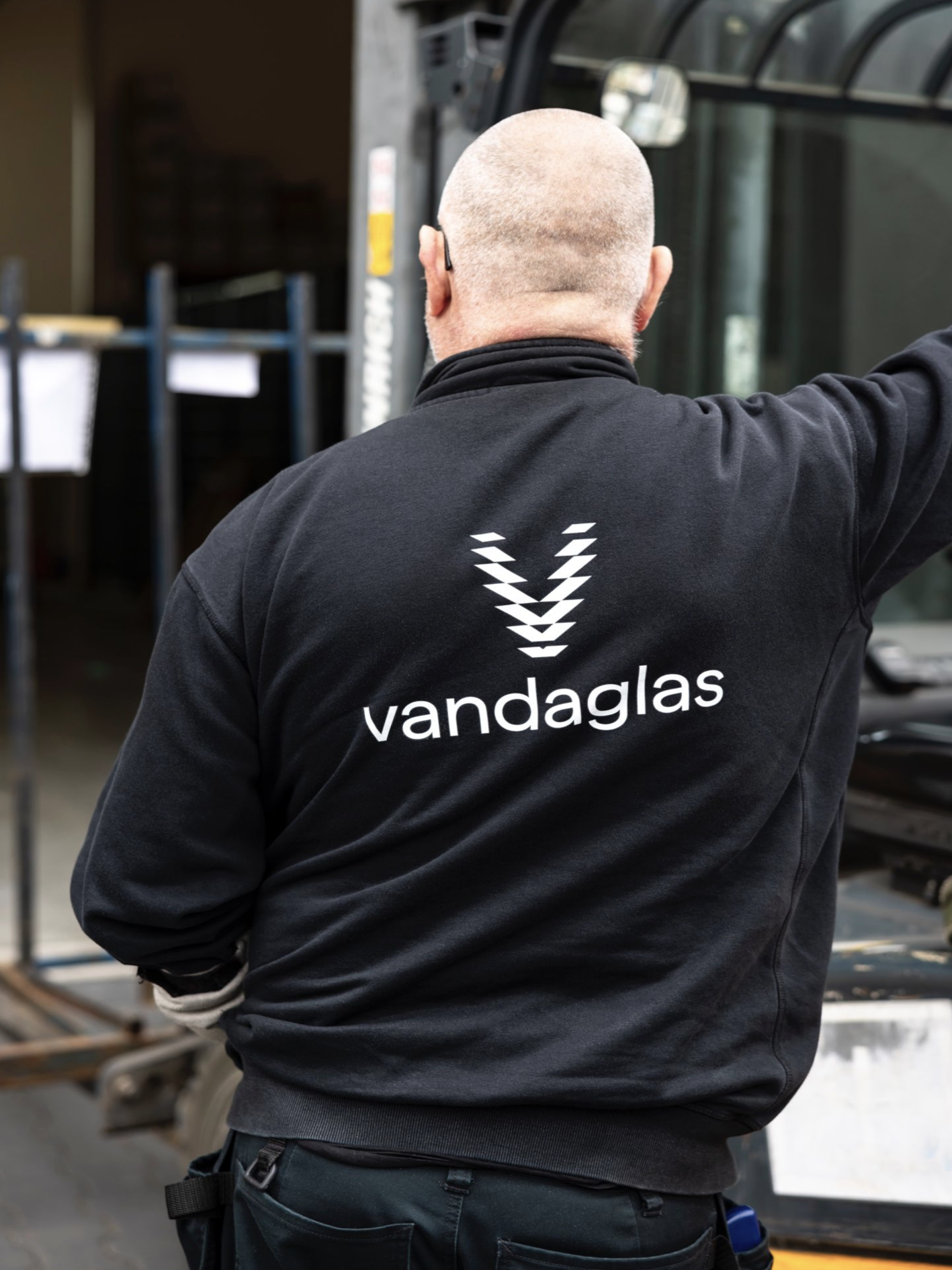 Ein Mann mit einem „vandaglas“-Pullover und einem Symbol auf dem Rücken, der von hinten gesehen wird.