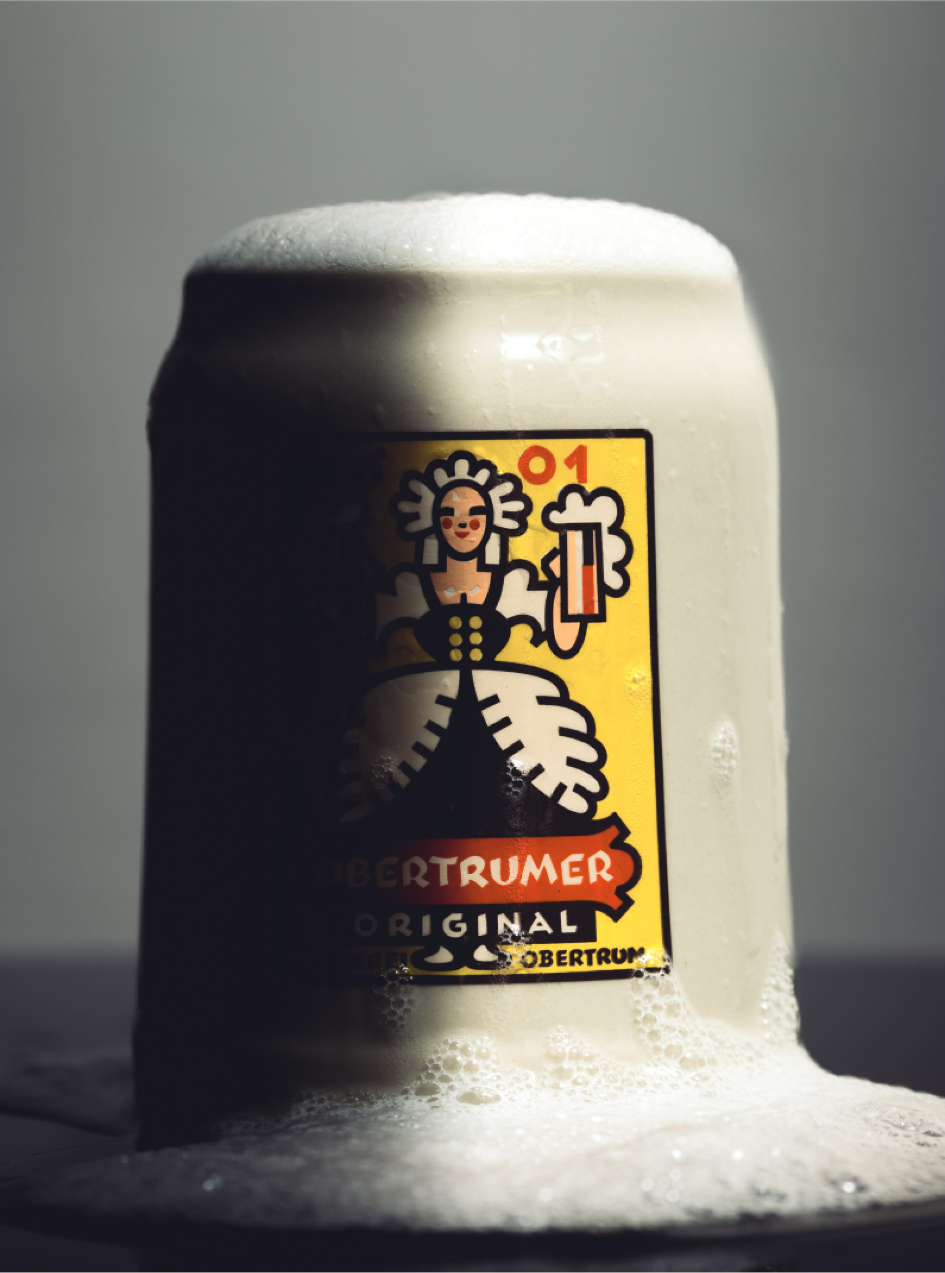 Ein Krug OBERTRUMER Original Bier mit Schaum läuft über. Das Etikett zeigt ein Mädchen und eine Maß Bier.