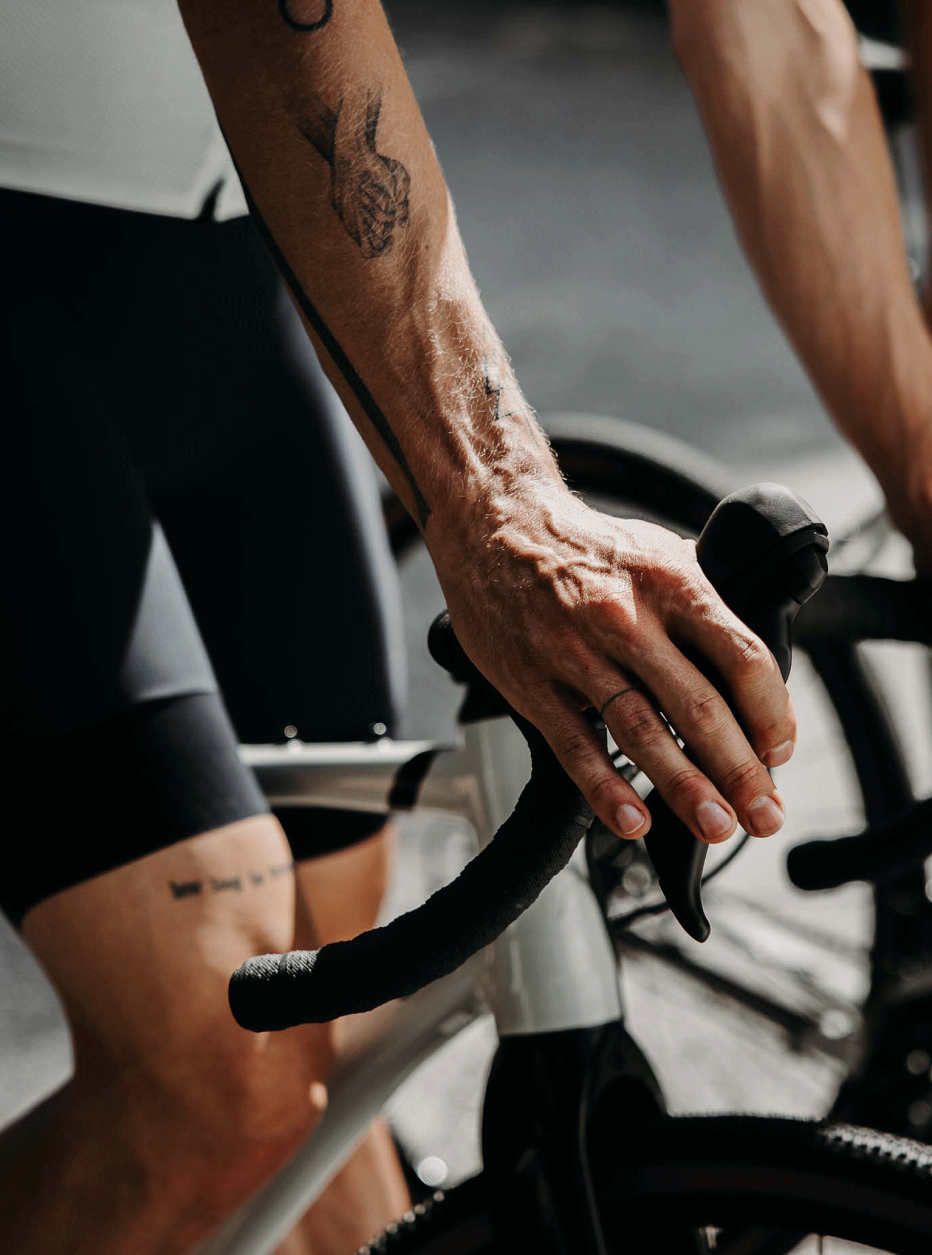 Nahaufnahme eines Radfahrers mit Tätowierungen, der einen weißen Rennradlenker mit schwarzen Griffen hält.