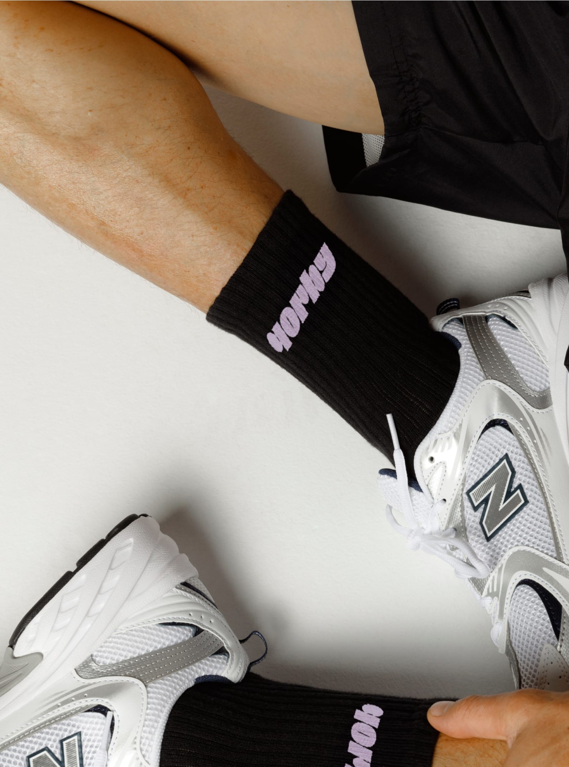 Nahaufnahme: Person mit schwarzen "Yorby"-Socken und weißen New Balance-Schuhen.