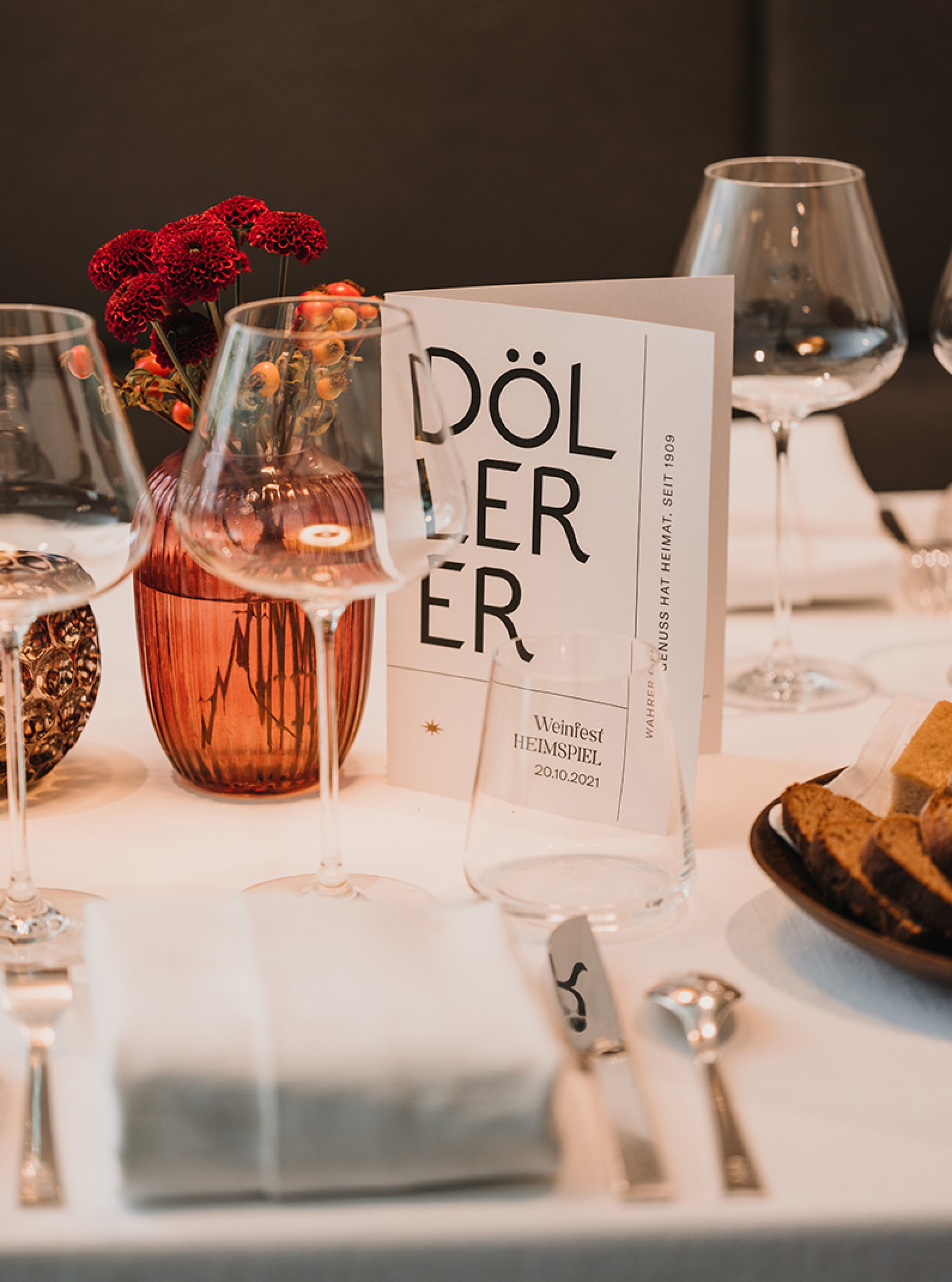 Ein gedeckter Tisch mit Blumen, Gläsern und einer Karte mit der Aufschrift "DÖLLER". "Weinfest Heimspiel 20.10.2021".