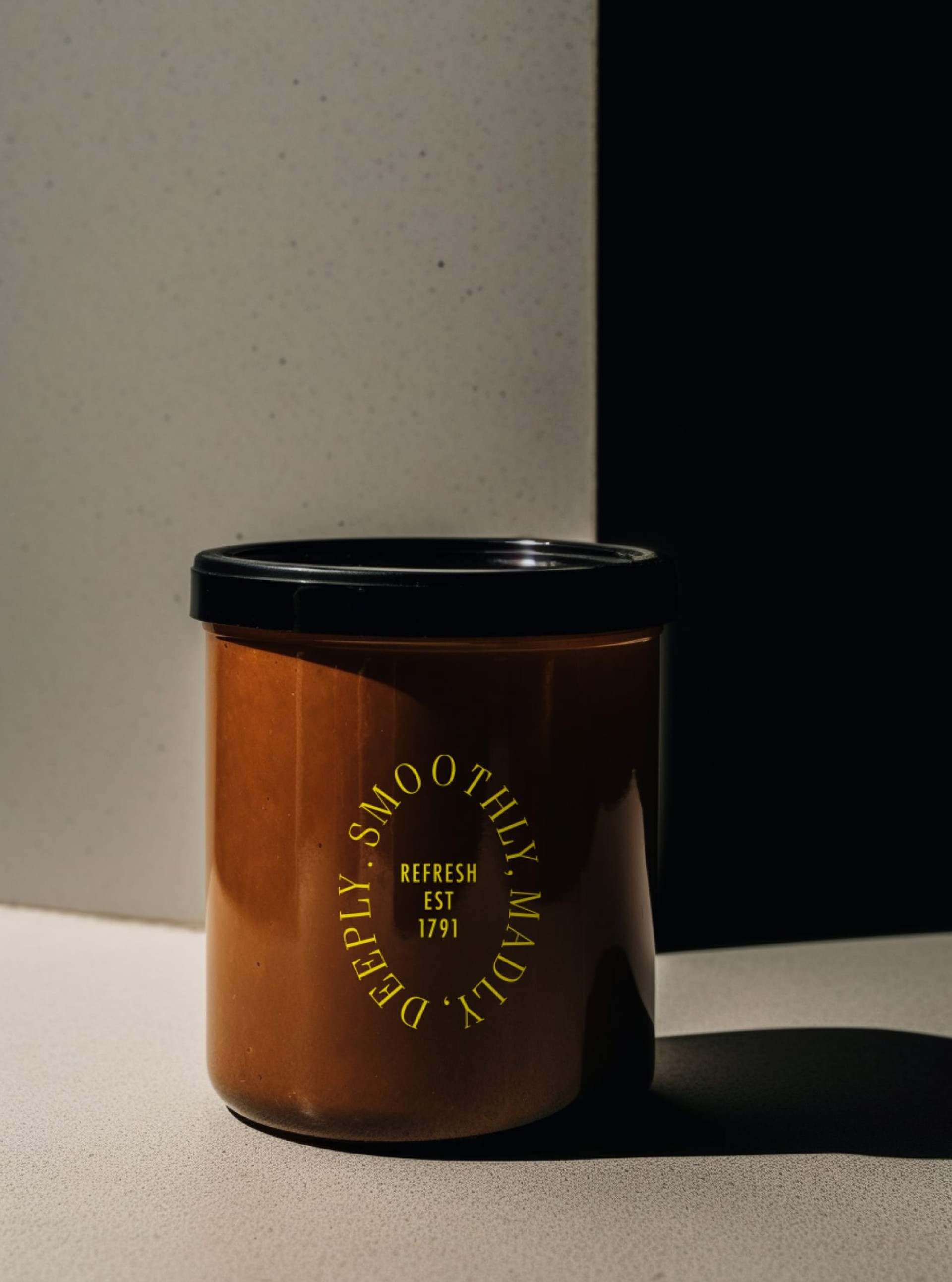 Brauner Behälter mit schwarzem Deckel. Gelbe Schrift: "DEEPLY. SMOOTHLY. MADLY. REFRESH EST 1791".