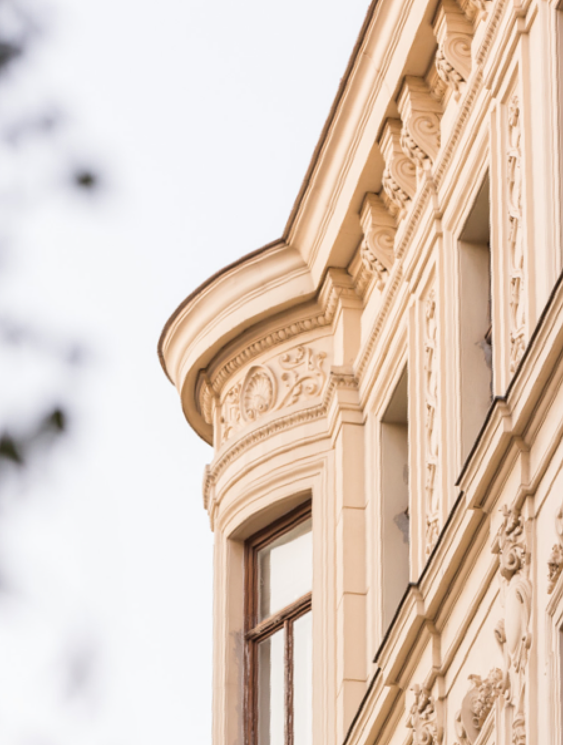 Detailaufnahme eines cremefarbenen, verzierten Gebäudes mit Fenstern und architektonischen Schnörkeln.