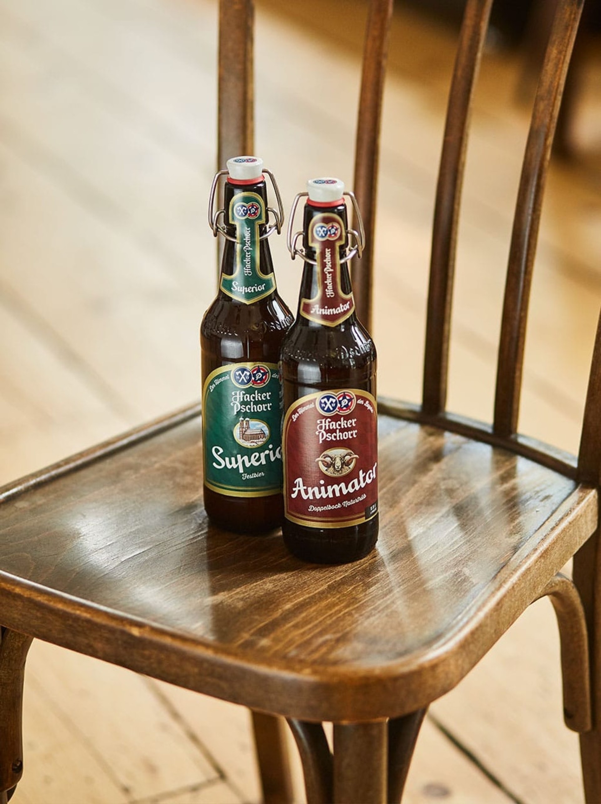 Zwei Hacker Pschorr Bierflaschen ("Superior", "Animator") stehen auf einem Holzstuhl.