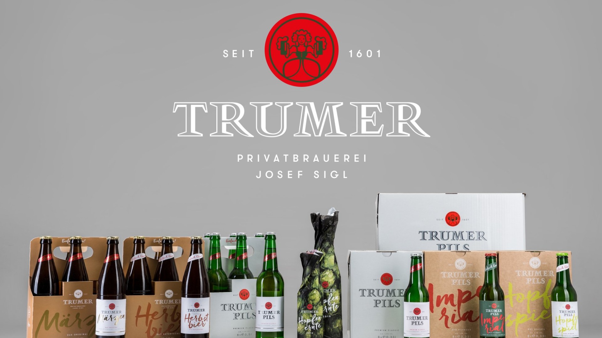 Mehrere Trumer Brauerei-Flaschen und -Kartons mit Text. Oben steht "TRUMER PRIVATBRAUEREI JOSEF SIGL SEIT 1601".