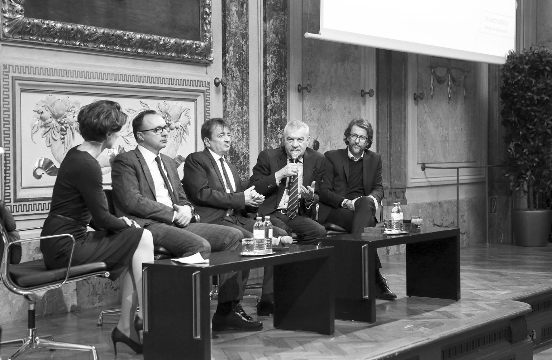 Schwarzweißfoto einer Podiumsdiskussion mit fünf Personen auf einer Bühne.
