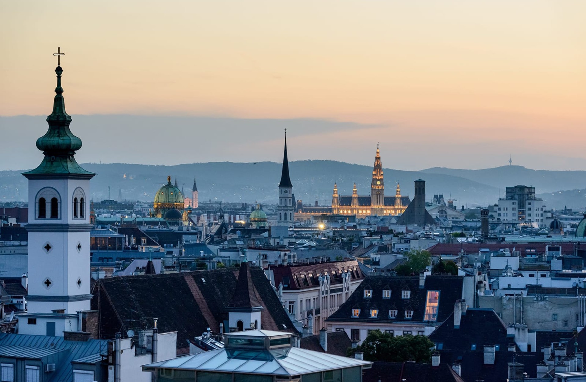 Blick auf Wien mit Kirchtürmen, Kuppeln und Stadthalle bei Dämmerung.