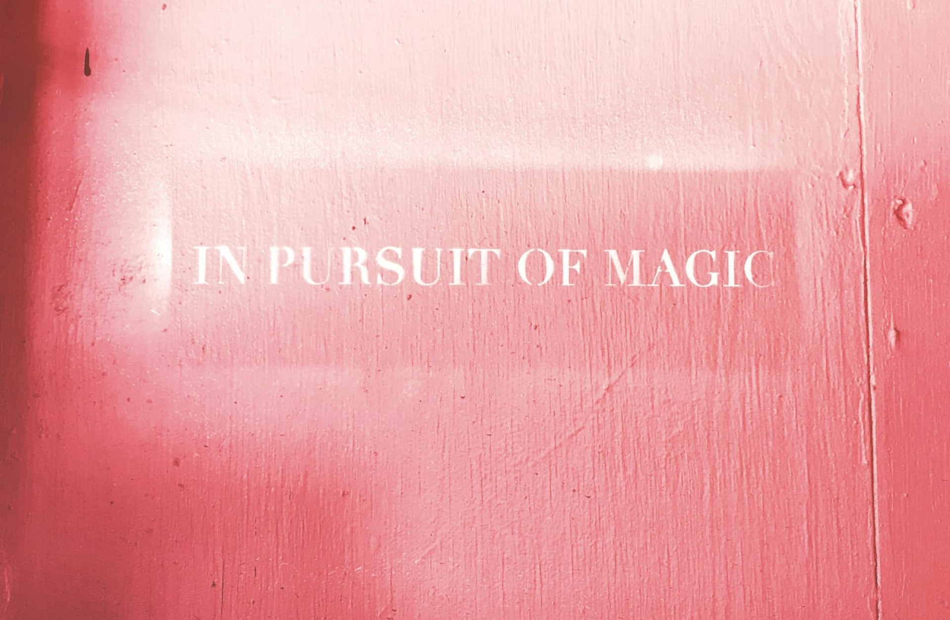 Rosa bemalte Tür mit dem Text "IN PURSUIT OF MAGIC" in weißer Schrift.