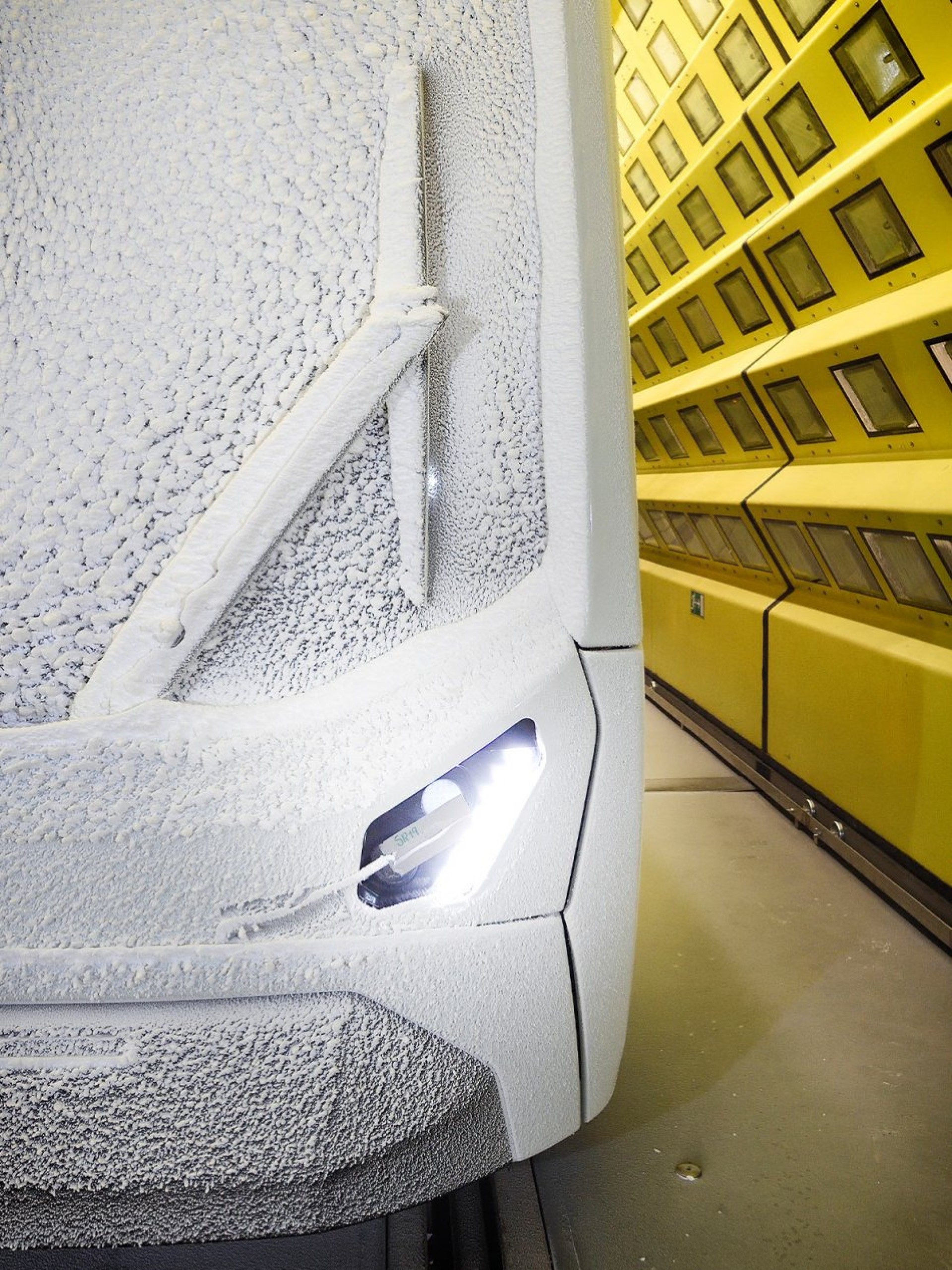 Eine Nahaufnahme eines weißen Autos mit Eis bedeckt, das in einem gelben Raum mit quadratischen Lichtern steht.