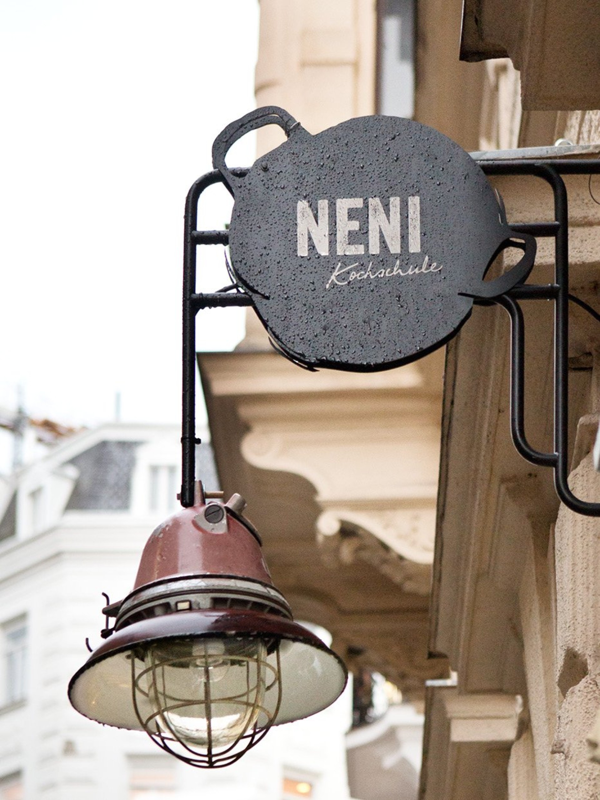 Außenaufnahme des Schildes "Neni Kochschule" in Form eines Topfes und einer alten Lampe.