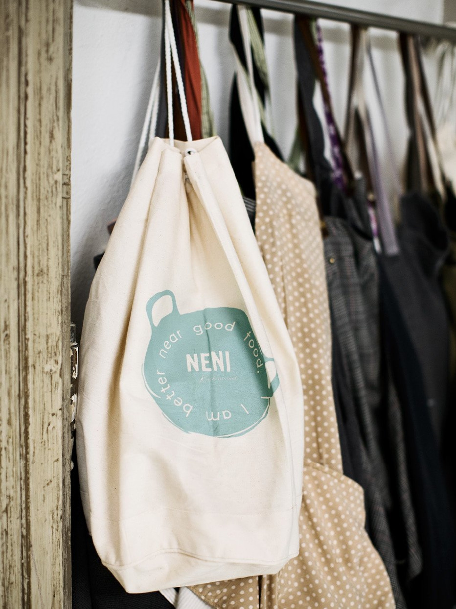 Ein Beutel mit "Neni near good food I am better"-Logo hängt an einer Kleiderstange.