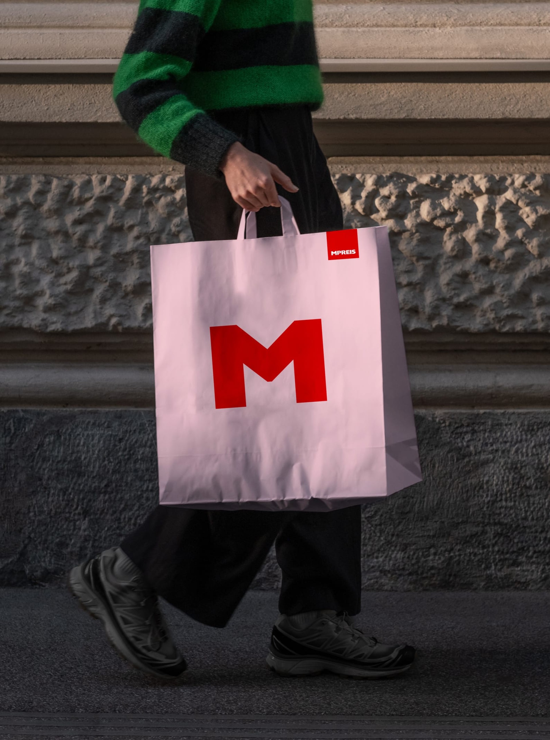 Eine Person mit einer rosa MPREIS-Einkaufstasche mit einem großen roten M-Logo.