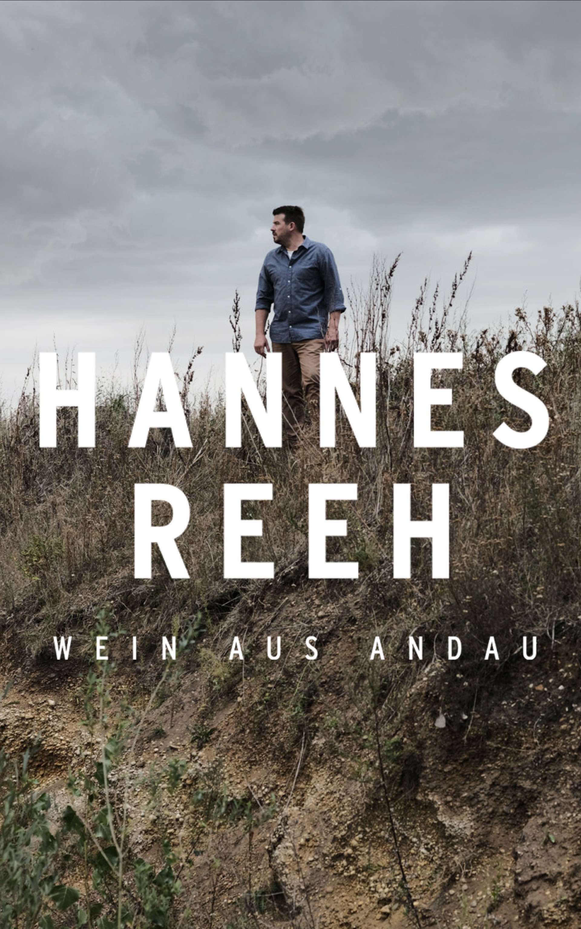 Ein Mann steht vor trockenem Gras. Text sagt: "Hannes Reeh, Wein aus Andau".
