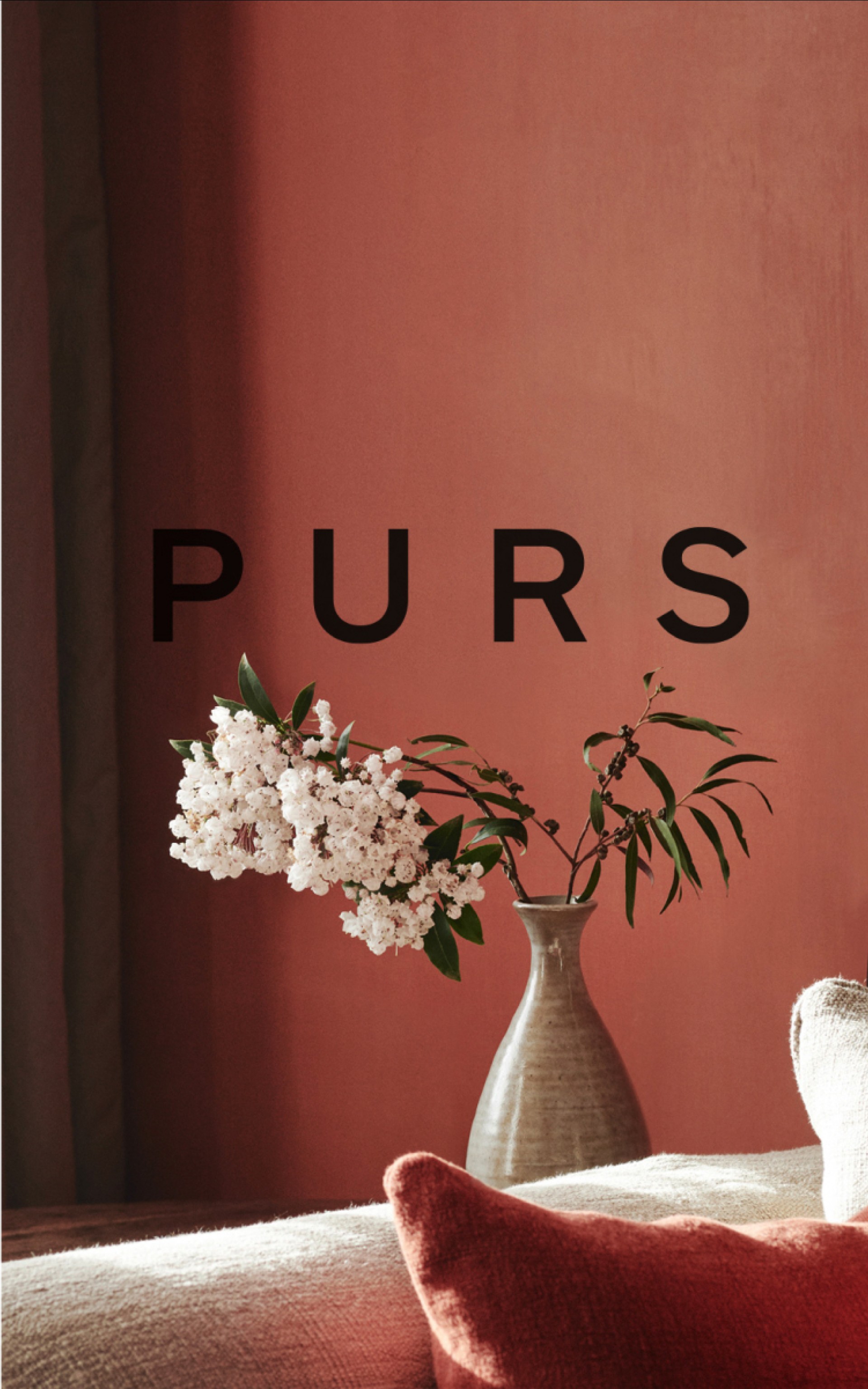Ein Blumenstrauß in einer Vase steht vor einer korallenroten Wand mit dem Text "PURS".