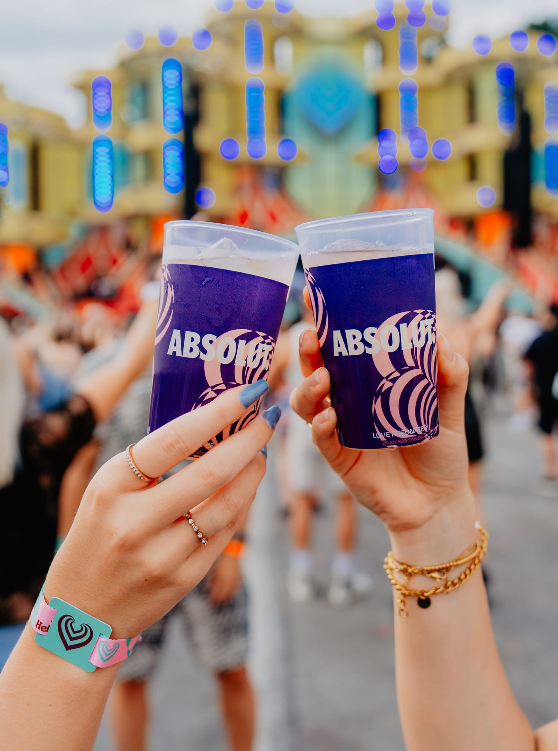 Zwei Hände halten "ABSOLUT"-Getränke vor einer Menschenmenge und einer Bühne.