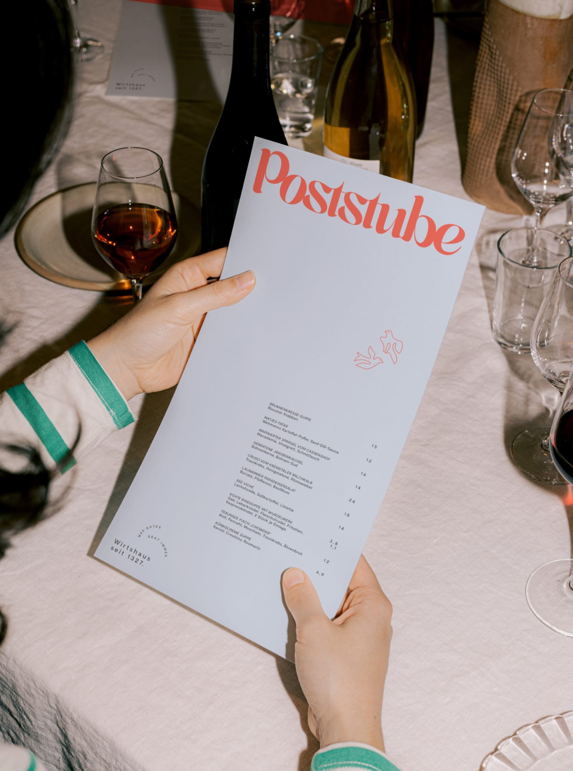 Person hält Menü "Poststube". Tisch mit Gläsern, Flaschen. "Wirtshaus seit 1327" steht auf dem Menü.