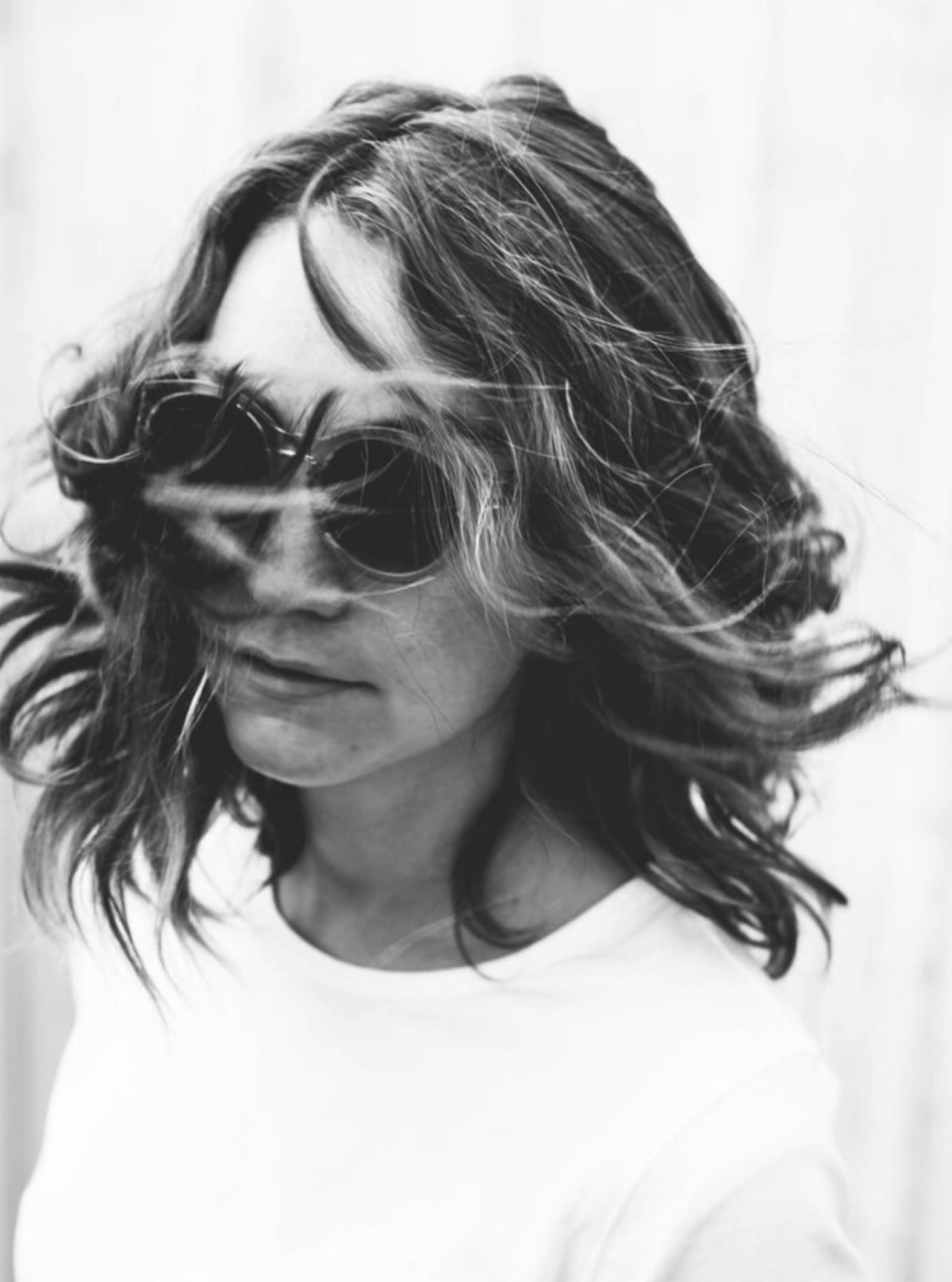 Eine Frau mit Sonnenbrille und wehendem Haar in einem Schwarzweißfoto.