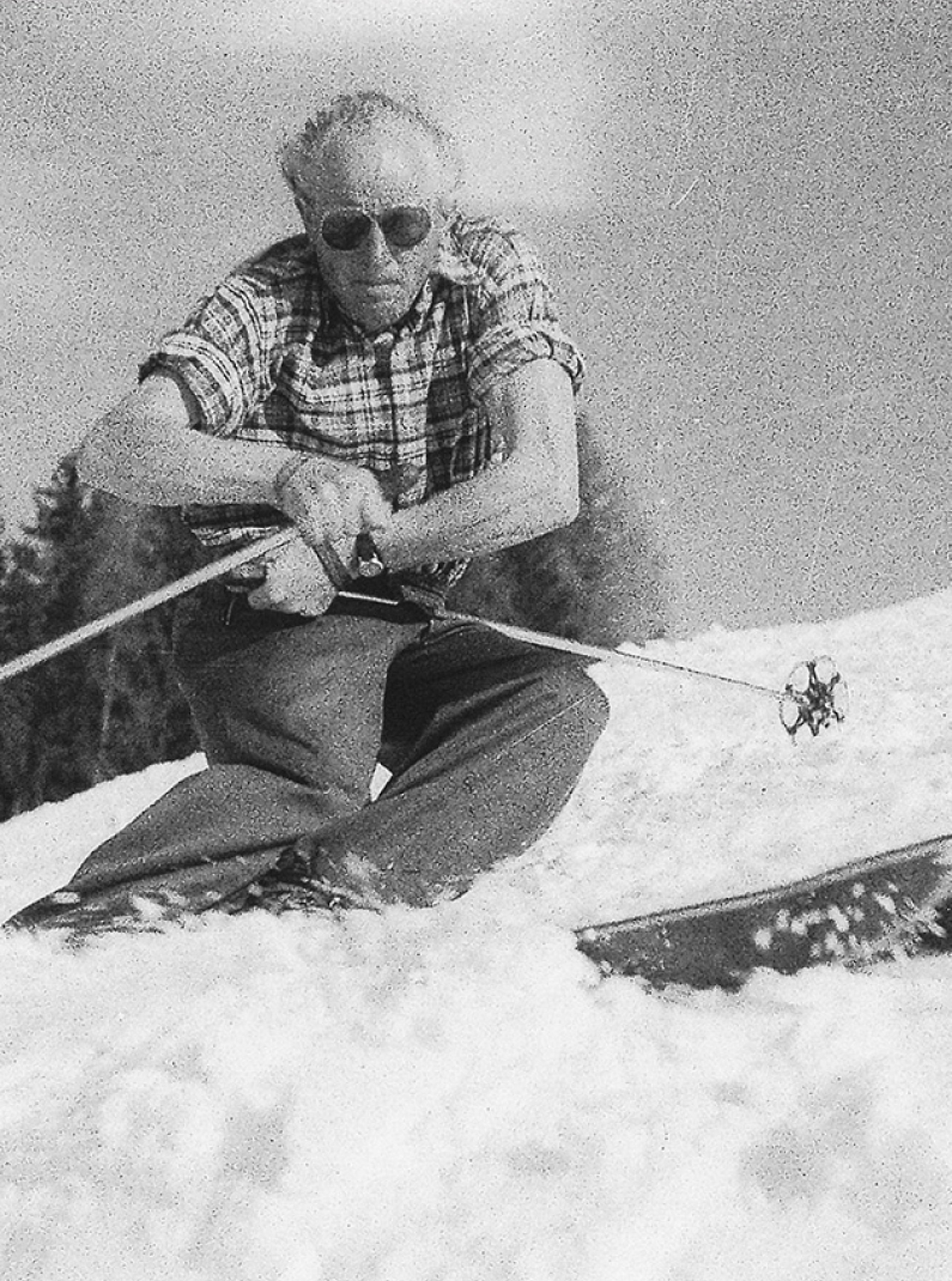 Ein Schwarz-Weiß-Foto einer älteren Person mit Sonnenbrille, die auf Skiern sitzt und Skistöcke hält.