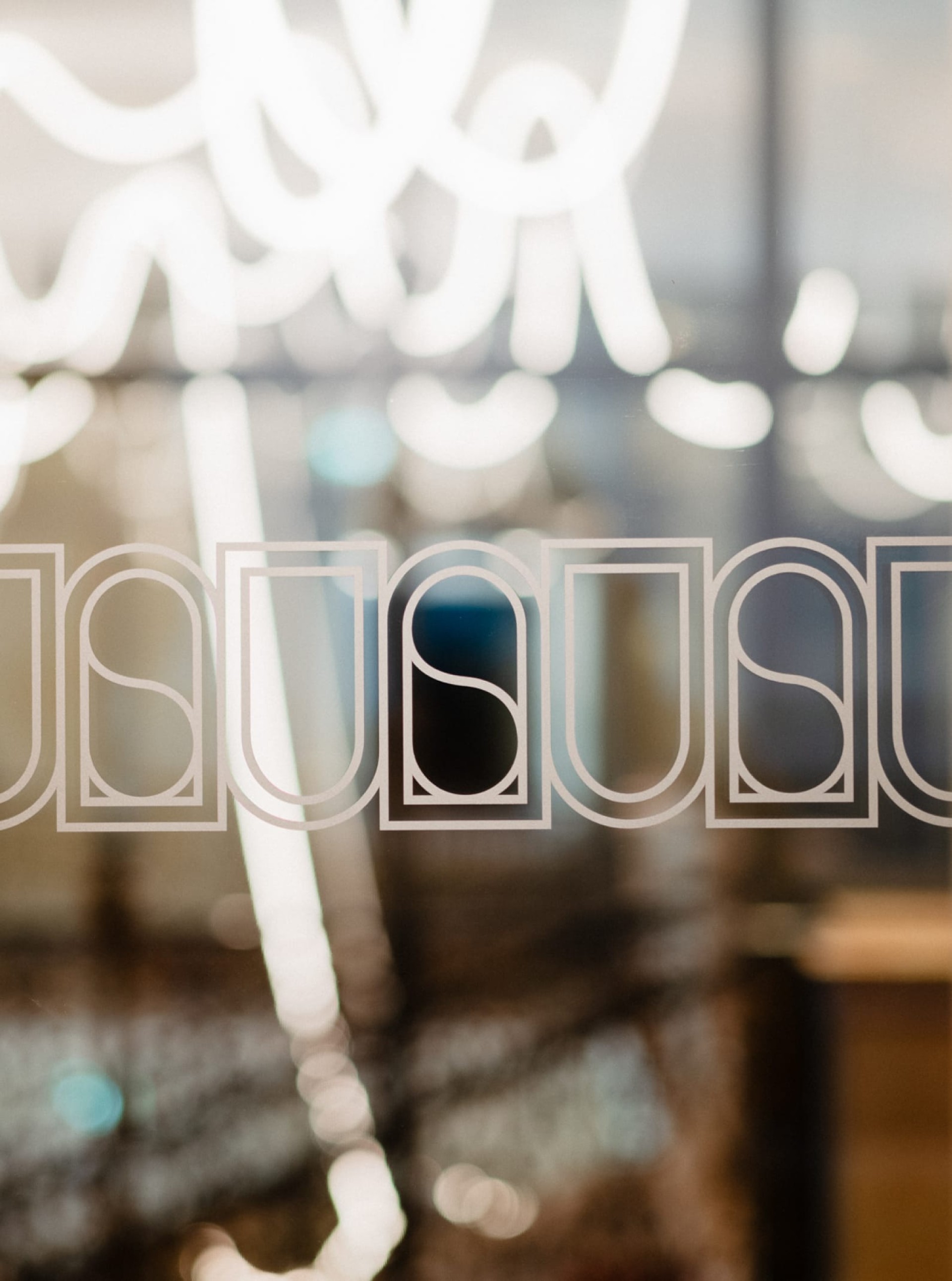 "USUAL" Schriftzug auf Glas, mit Bokeh-Lichtern im Hintergrund.