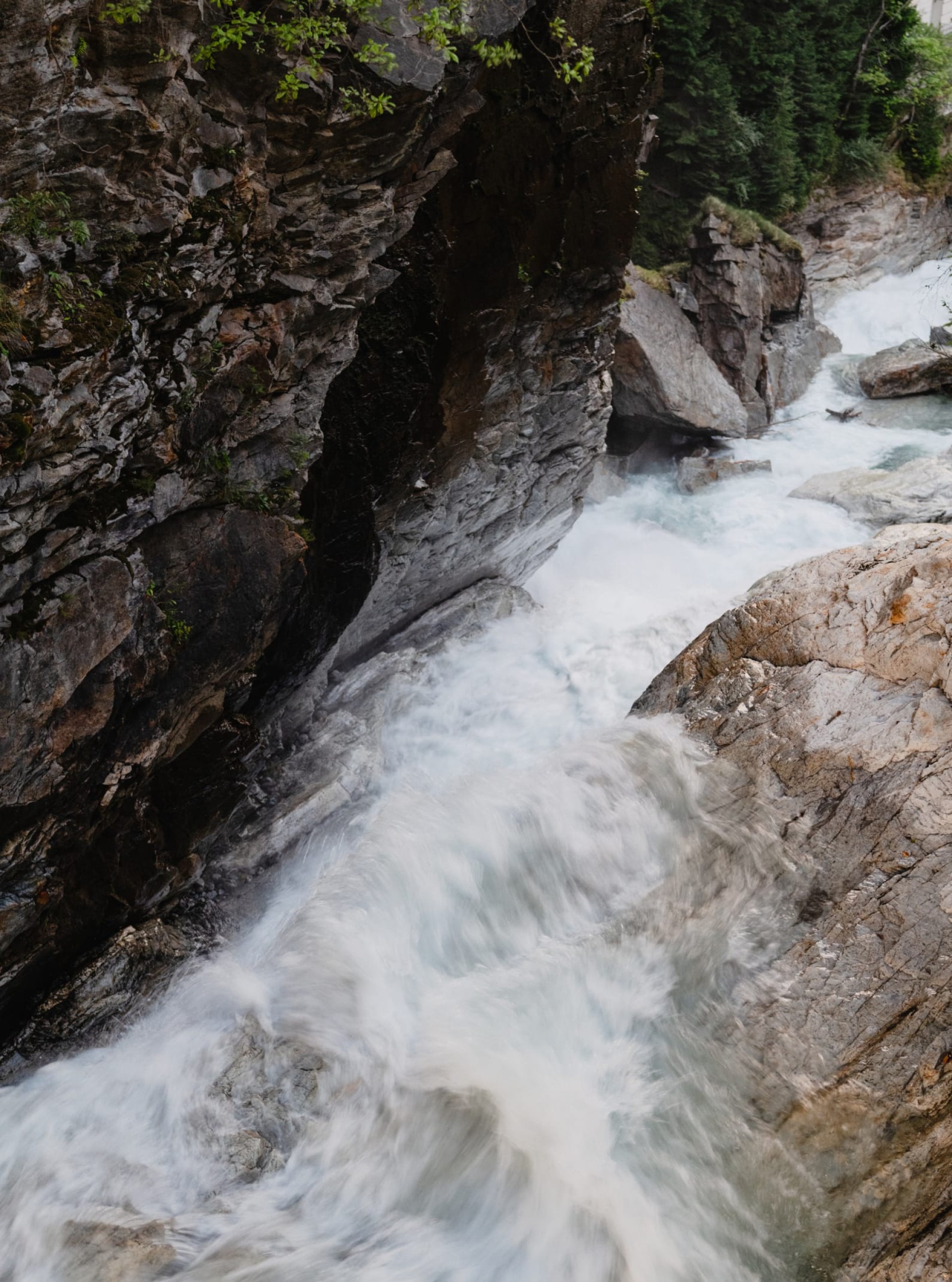 Ein Blick von oben auf einen Wasserfall, der durch graue Felsen fließt.