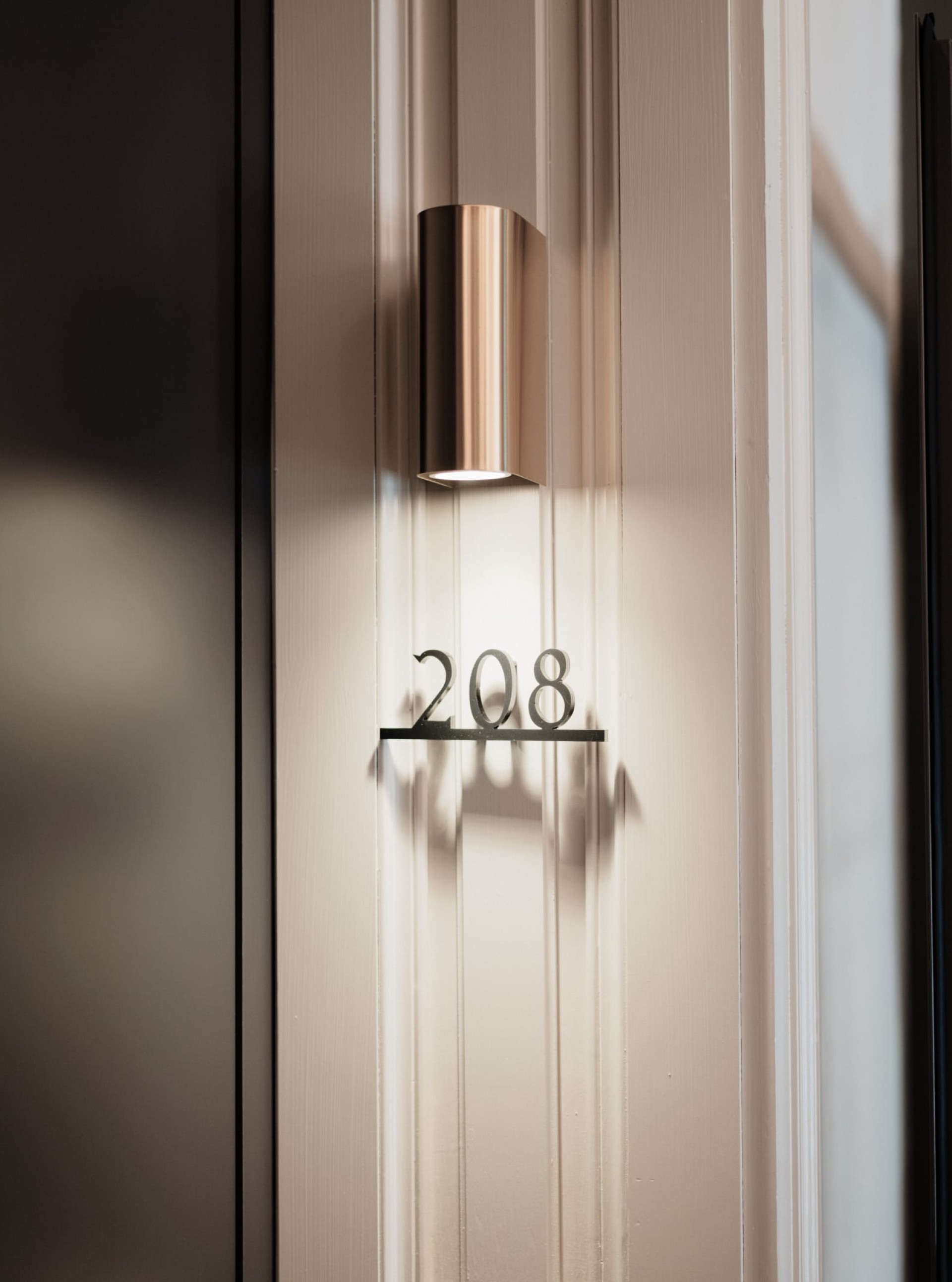 Nahaufnahme der Tür mit der Nummer 208, mit einer bronzefarbenen Wandleuchte darüber.