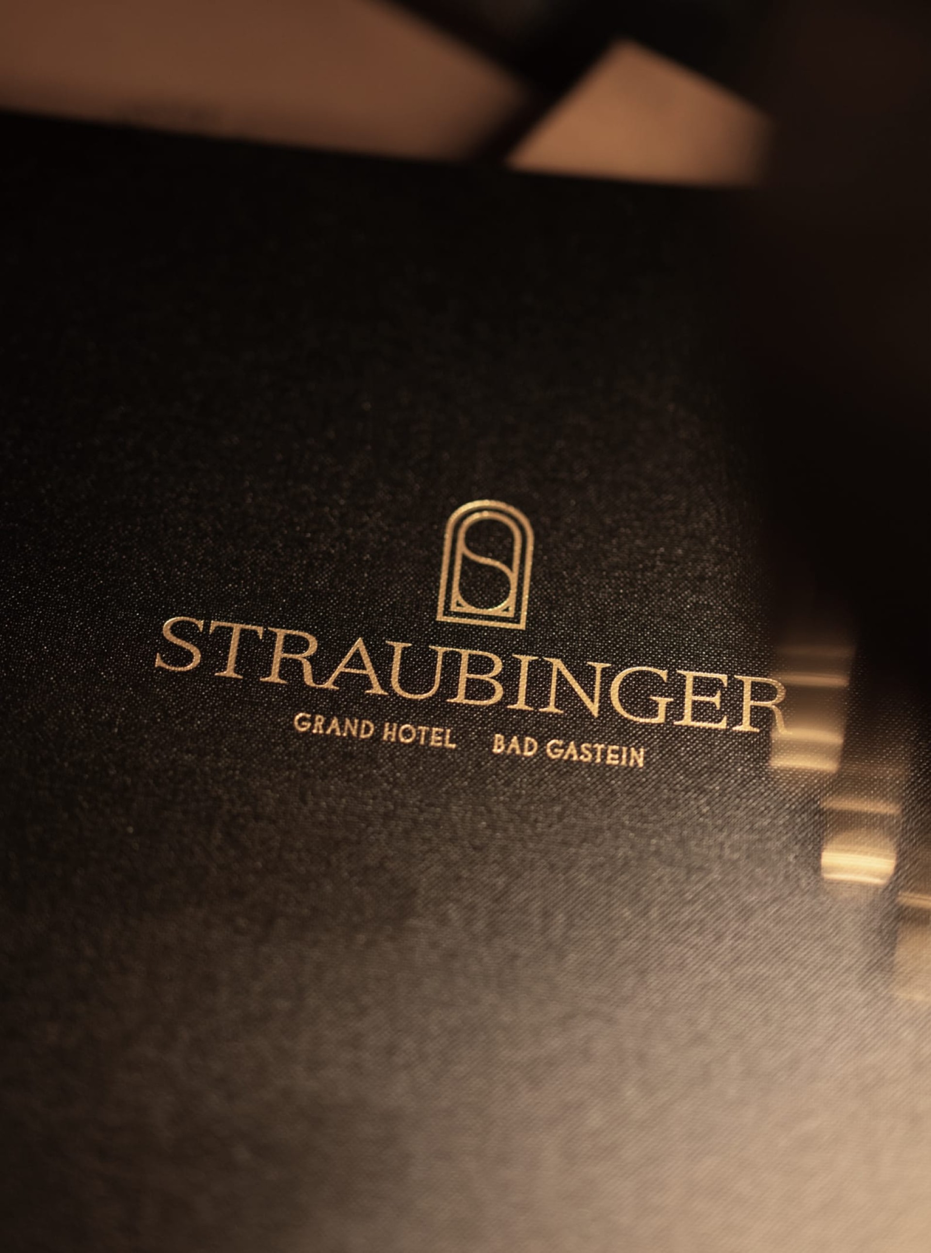 Nahaufnahme des goldenen Logos "STRAUBINGER GRAND HOTEL BAD GASTEIN" auf schwarzem Material.