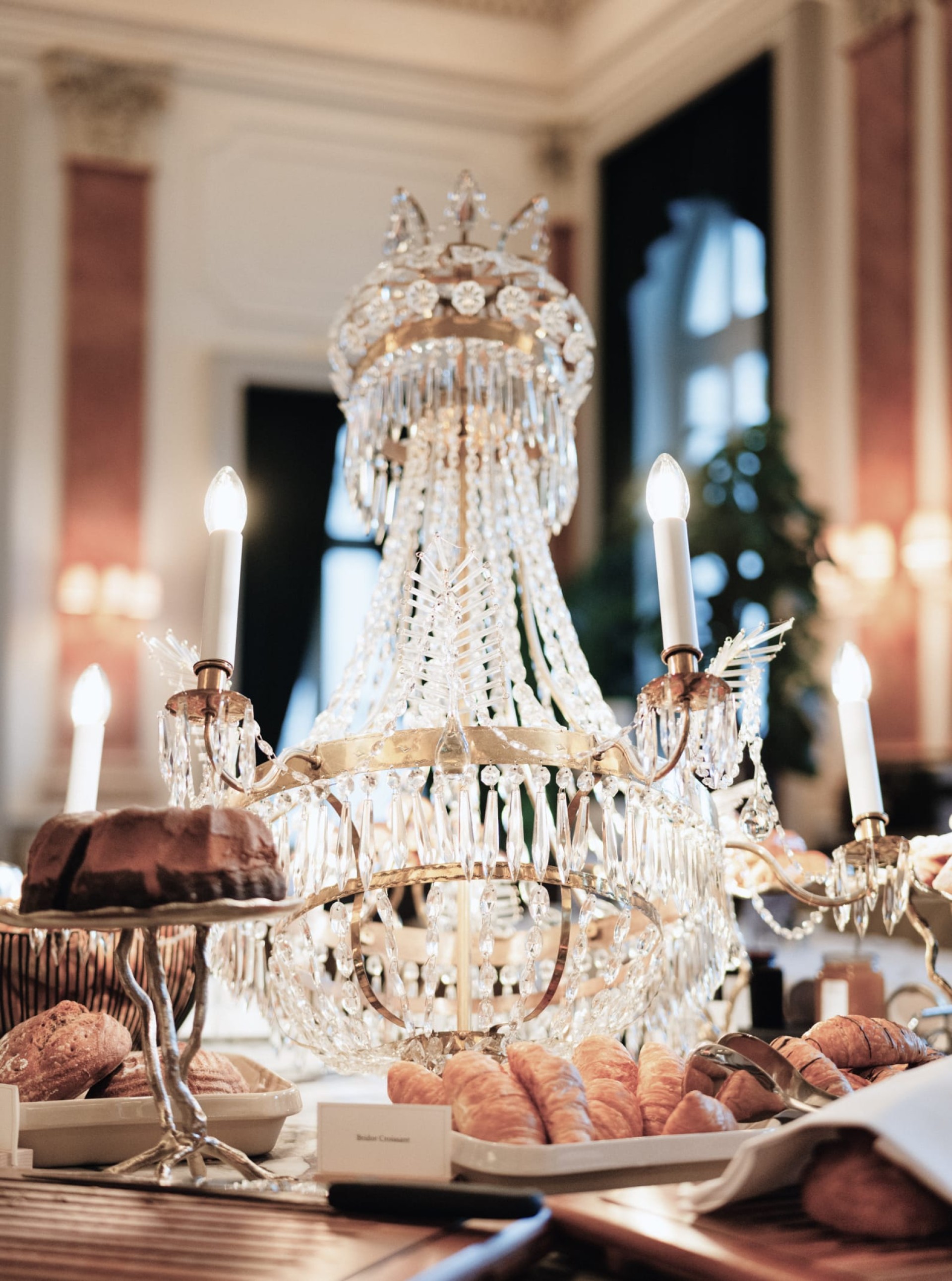 Nahaufnahme eines Kronleuchters über Croissants und einem Kuchen.