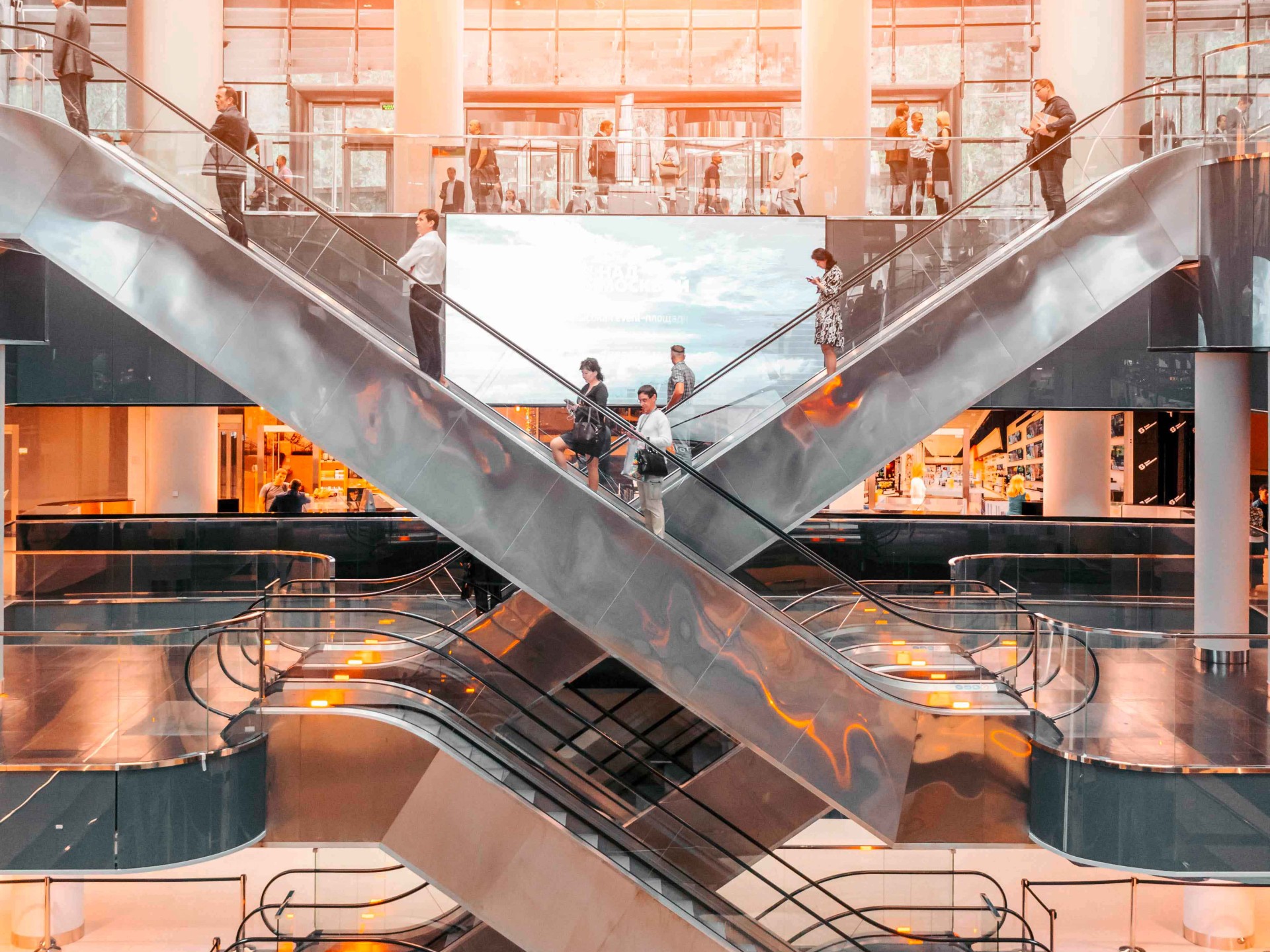 Innenansicht eines Gebäudes mit mehreren Rolltreppen und vielen Menschen.
