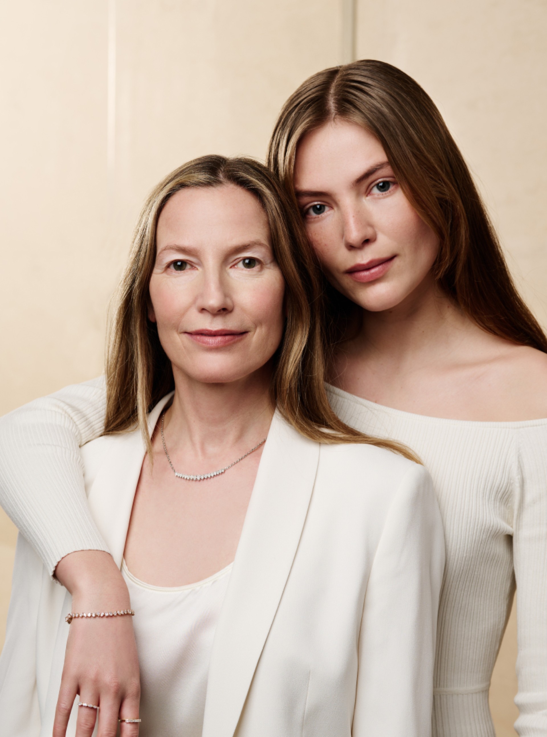 Zwei Frauen stehen nahe beieinander. Sie tragen Schmuck und weiße Kleidung.
