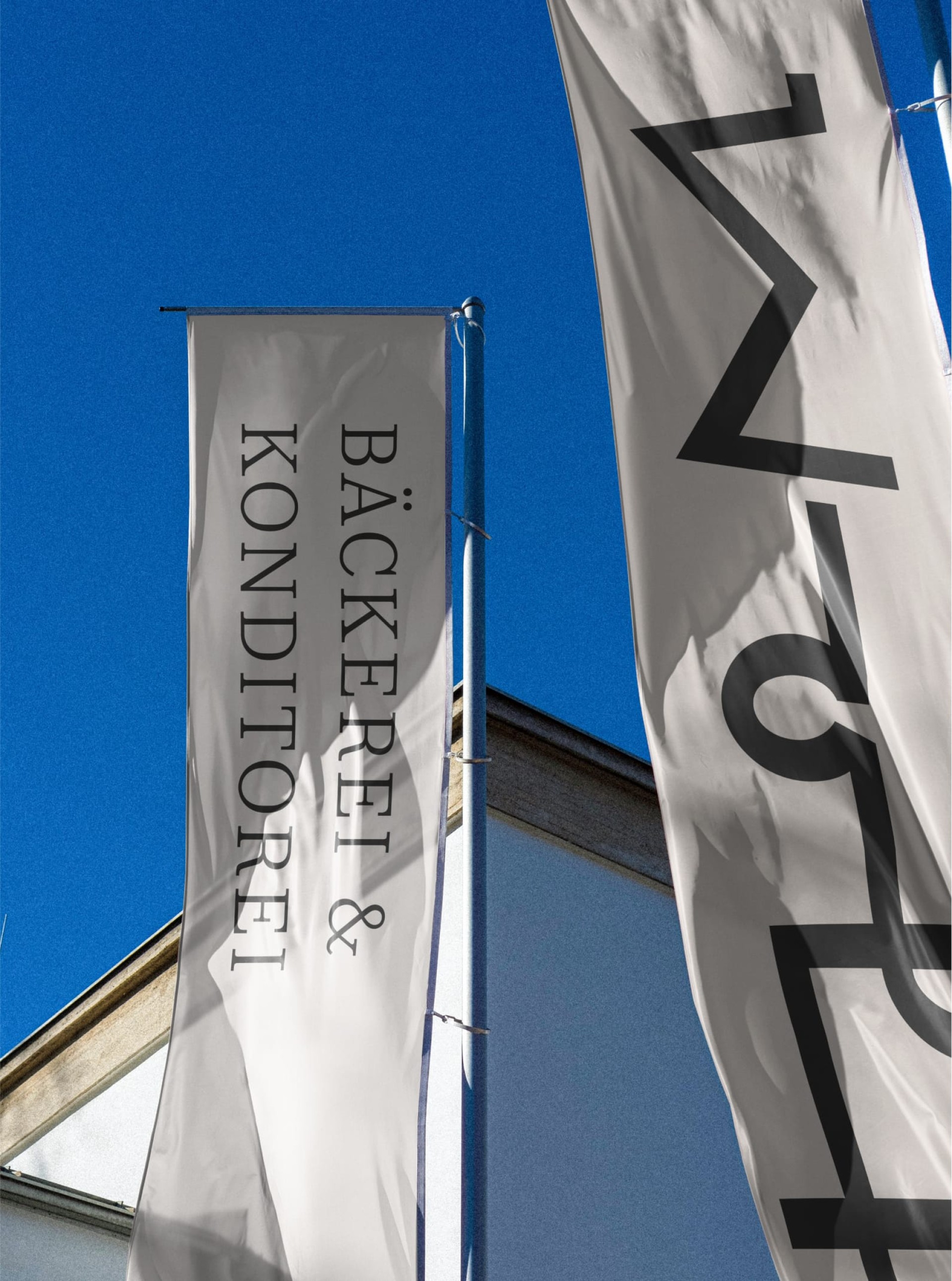 Weiße Fahnen mit Text „Bäckerei & Konditorei“ und einem abstrakten Logo gegen einen blauen Himmel.