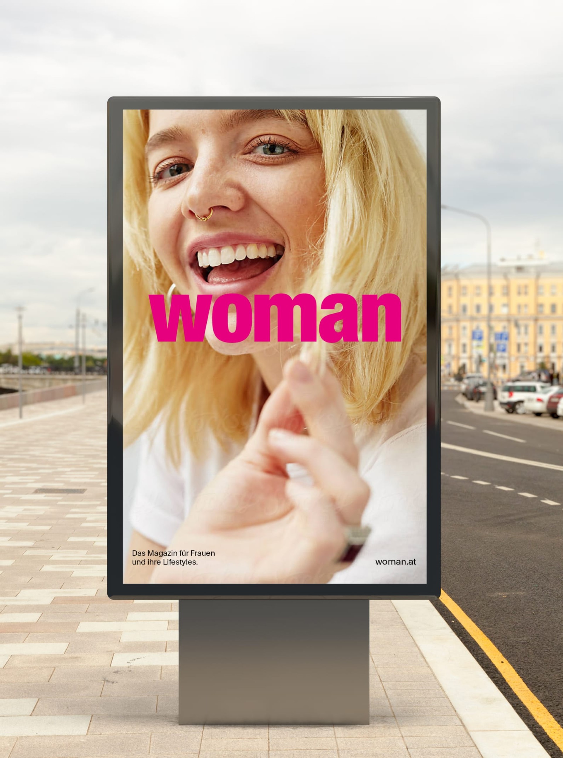 Ein hochformatiges Plakat zeigt eine lachende Frau und den Text "woman". Das Magazin für Frauen und ihre Lebensstile. woman.at