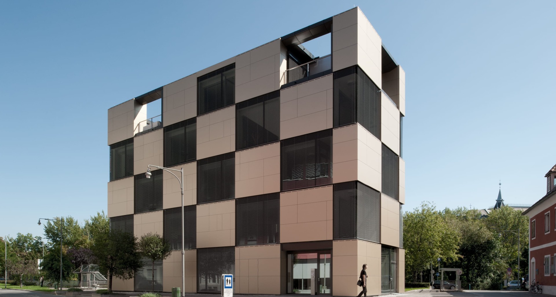Würfelförmiges Gebäude, helle und dunkle Quadrate bilden eine Fassade, ein blauer Himmel.