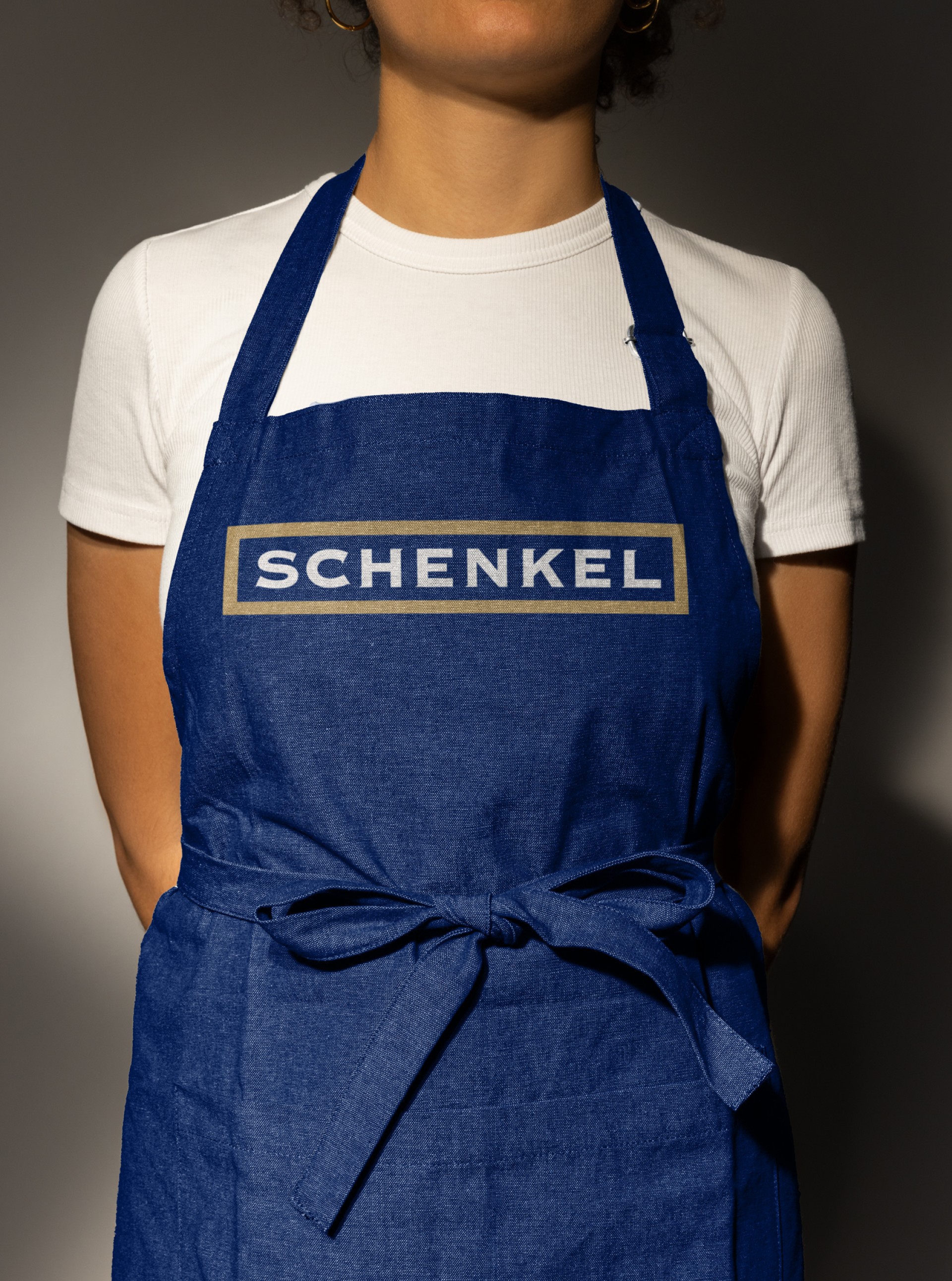 Eine Person, die eine blaue "Schenkel"-Schürze über einem weißen T-Shirt trägt.
