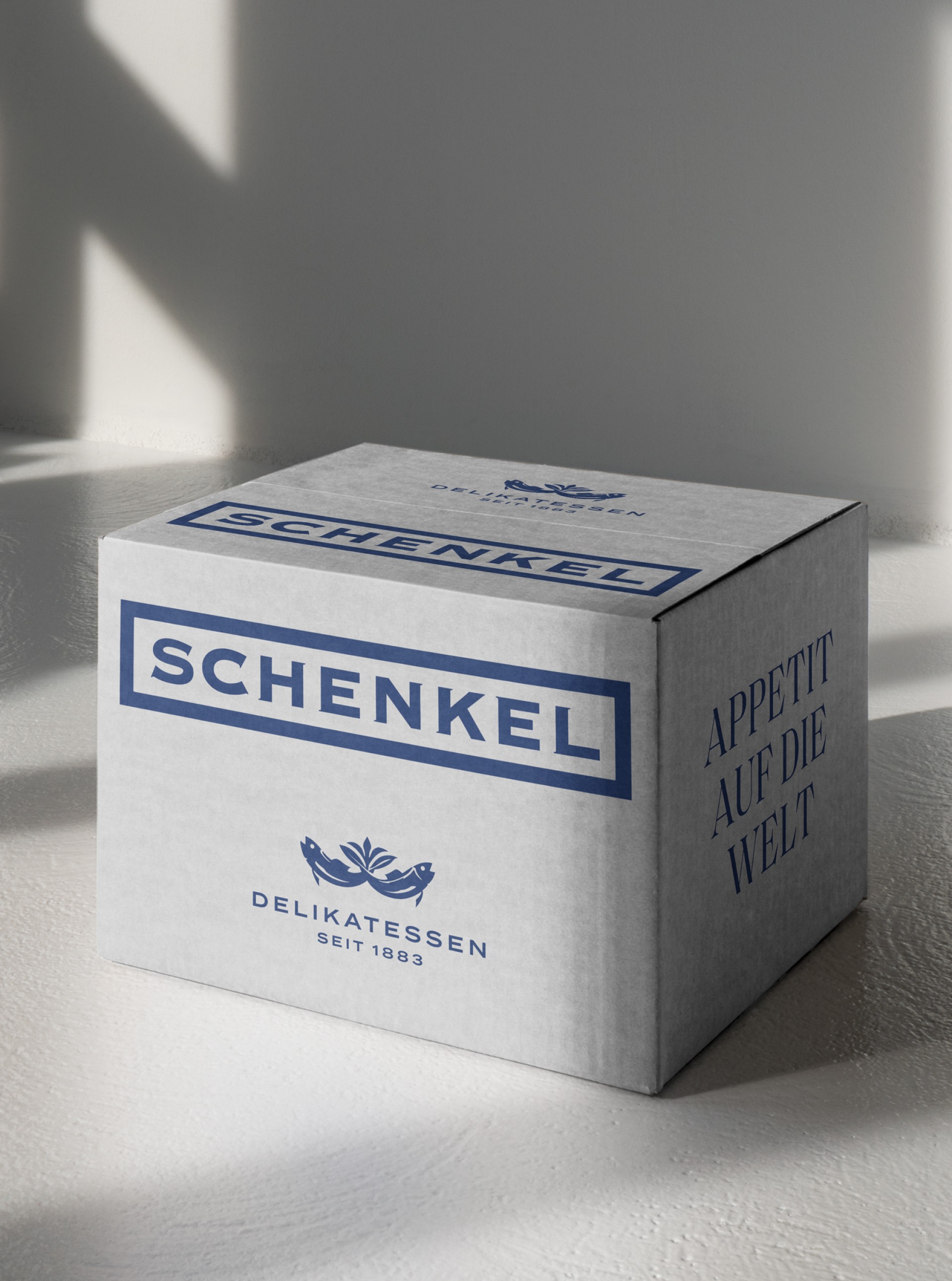 Ein quadratischer Karton der Marke Schenkel Delikatessen seit 1883 mit der Aufschrift Appetit auf die Welt.