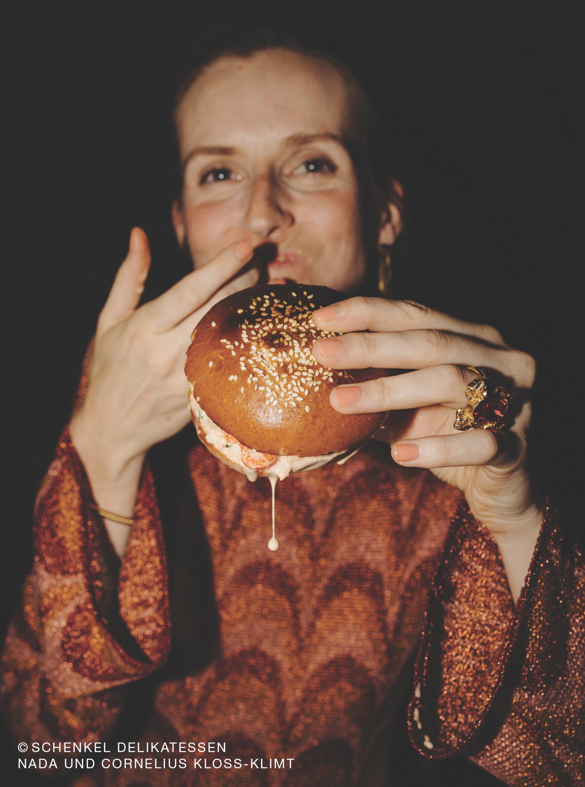 Frau isst Burger von Schenkel Delikatessen. Aufschrift: Nada und Cornelius Kloss-Klimt.