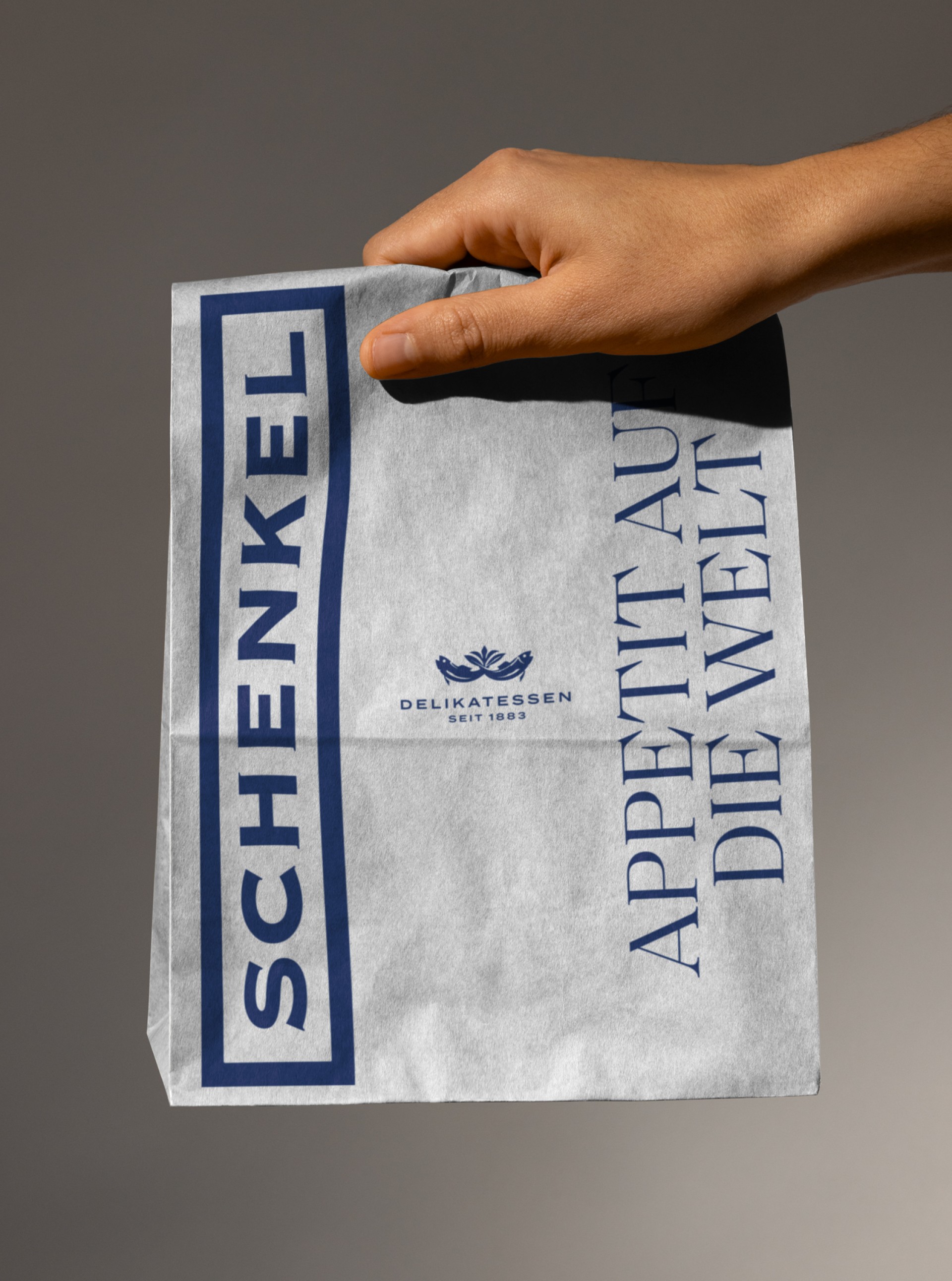 Eine Hand hält eine Schenkel-Delikatessen-Papiertüte mit der Aufschrift "Appetit auf die Welt".