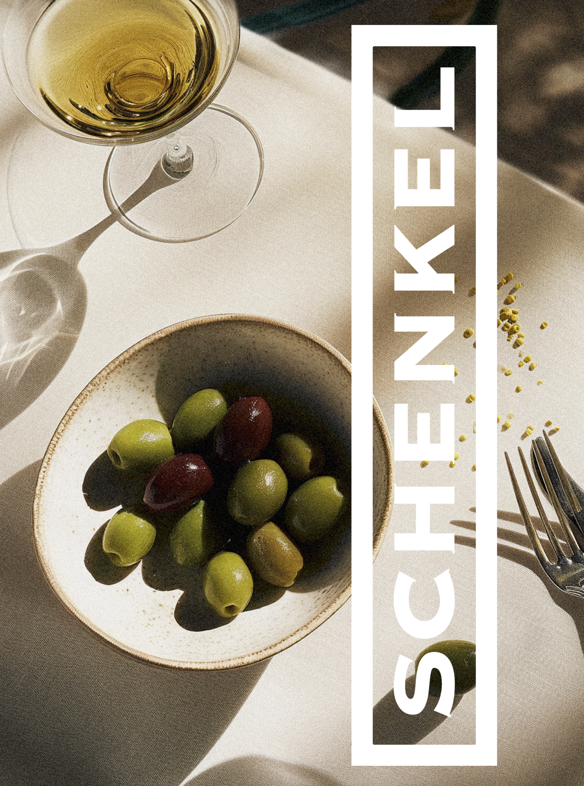 Stillleben mit Oliven in Schale, Glas Wein und Gabel. "SCHENKEL" in vertikalem Text.