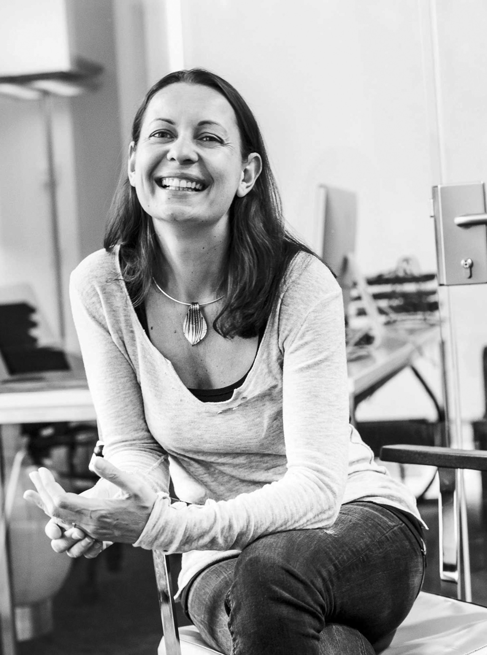 Eine Frau sitzt in einem Büro, lächelt und blickt in die Kamera.