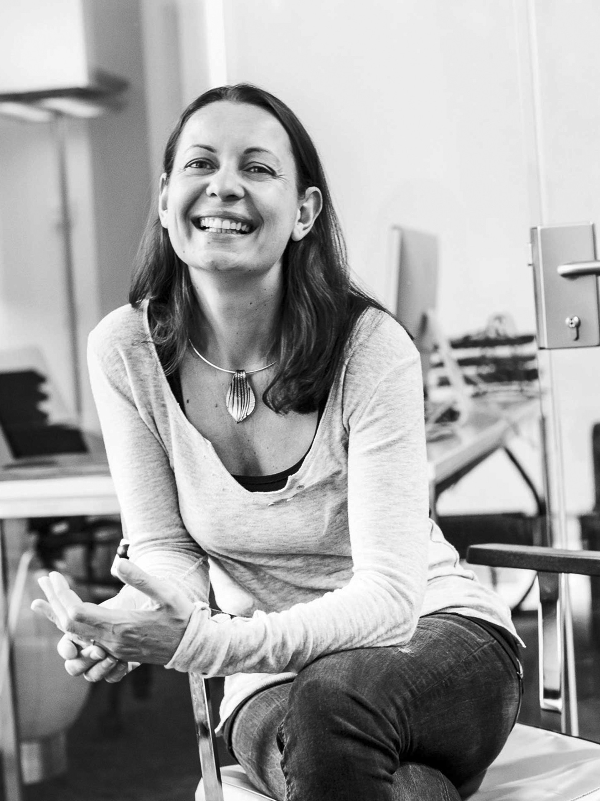 Eine Frau sitzt in einem Büro, lächelt und blickt in die Kamera.